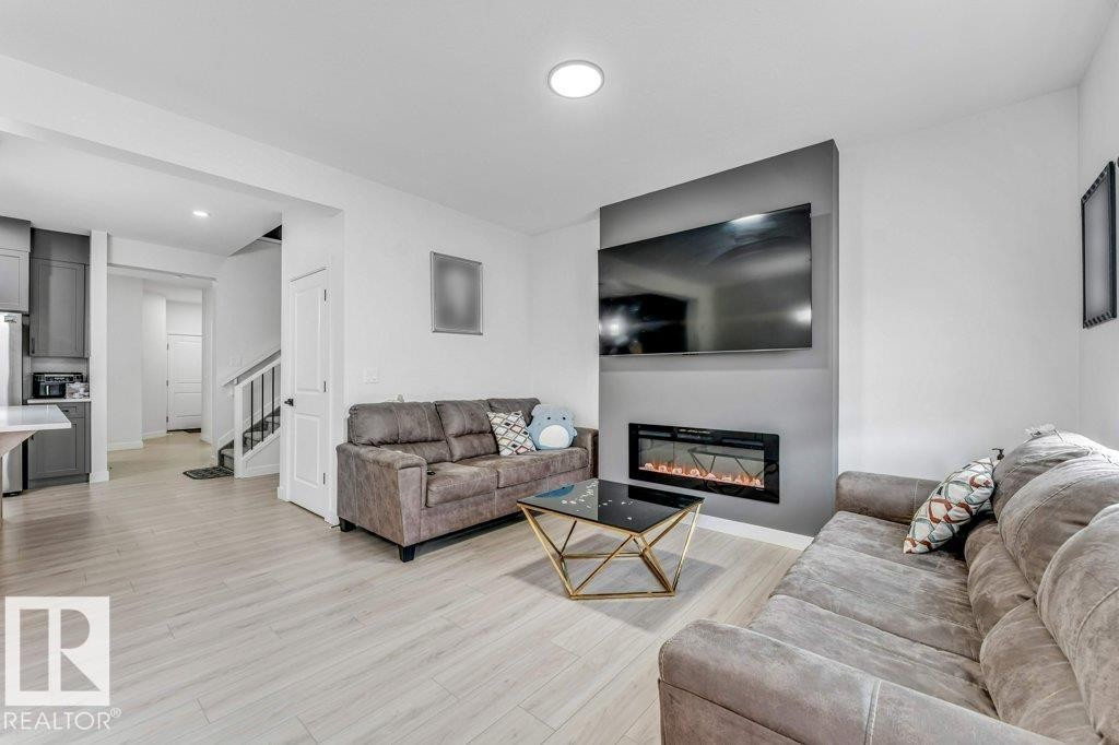 Modern living area featuring light wood-finish flooring, a contemporary electric fireplace, and a striking gray accent wall - 423 28 Street, Edmonton, AB