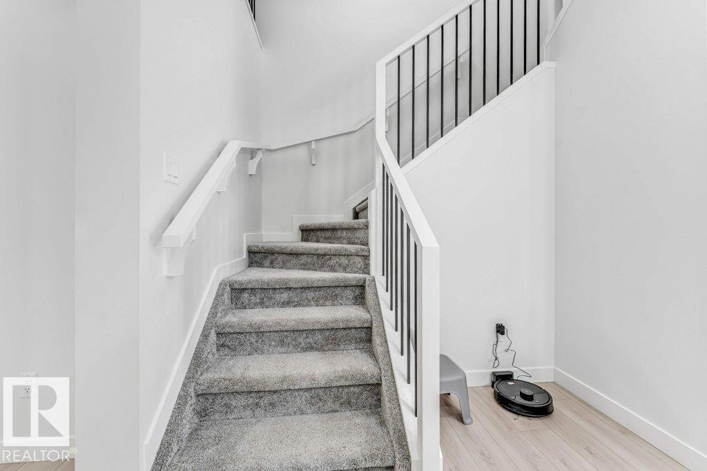 Modern staircase featuring carpeted treads, white risers, and a contemporary railing with black metal balusters and a white handrail - 423 28 Street, Edmonton, AB