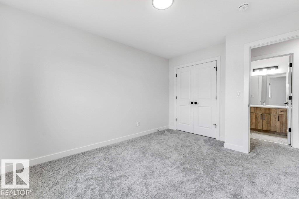 Spacious room featuring light gray carpeting, white walls, and a contemporary ceiling light fixture - 423 28 Street, Edmonton, AB