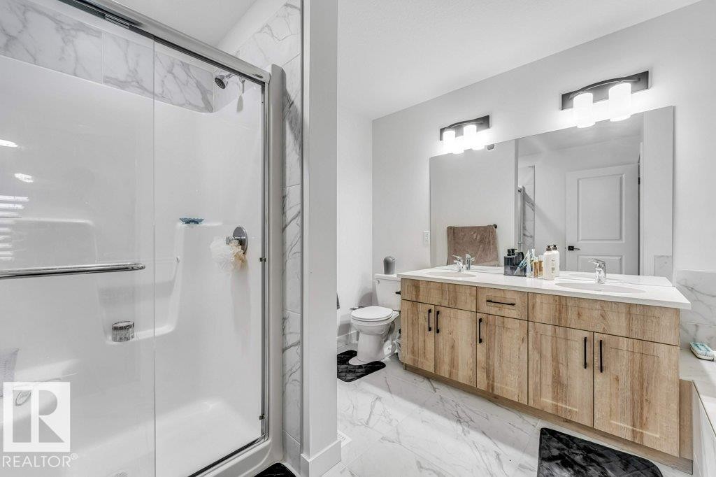 Contemporary bathroom featuring a spacious shower enclosure with clear glass doors, a dual-sink vanity with wood-finish cabinetry, a large wall-mounted mirror, and overhead lighting fixtures - 423 28 Street, Edmonton, AB
