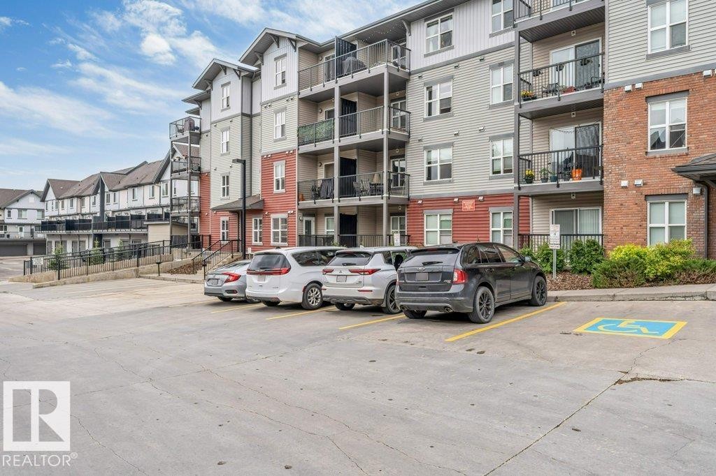 Multi-story apartment building featuring brick and siding exteriors, private balconies with black railings, and a ground-level parking area with paved surfaces - 401 667 Watt Boulevard, Edmonton, AB