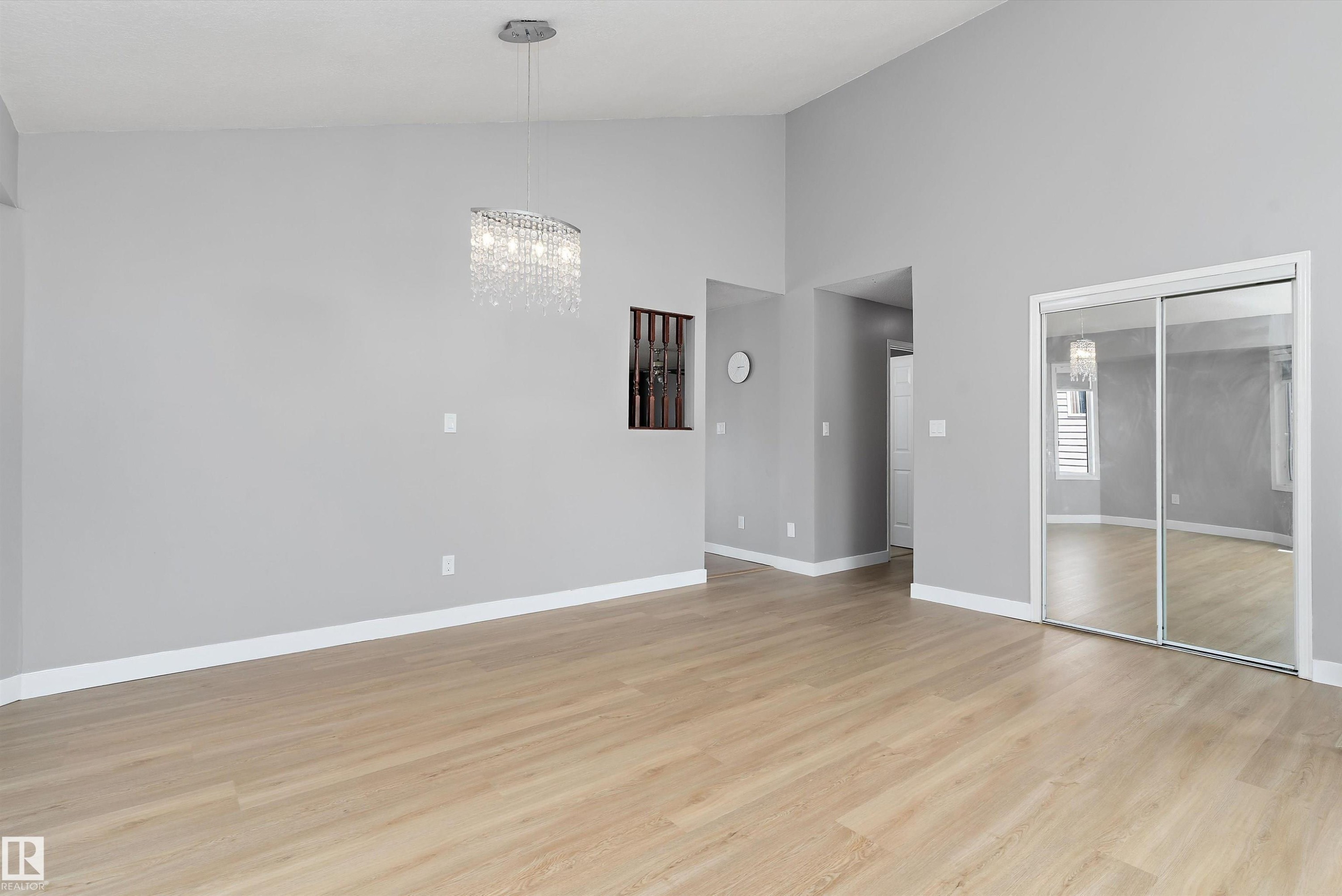 Spacious interior featuring light wood-finish flooring, vaulted ceilings, and a contemporary crystal chandelier - 14707 33 Street, Edmonton, AB