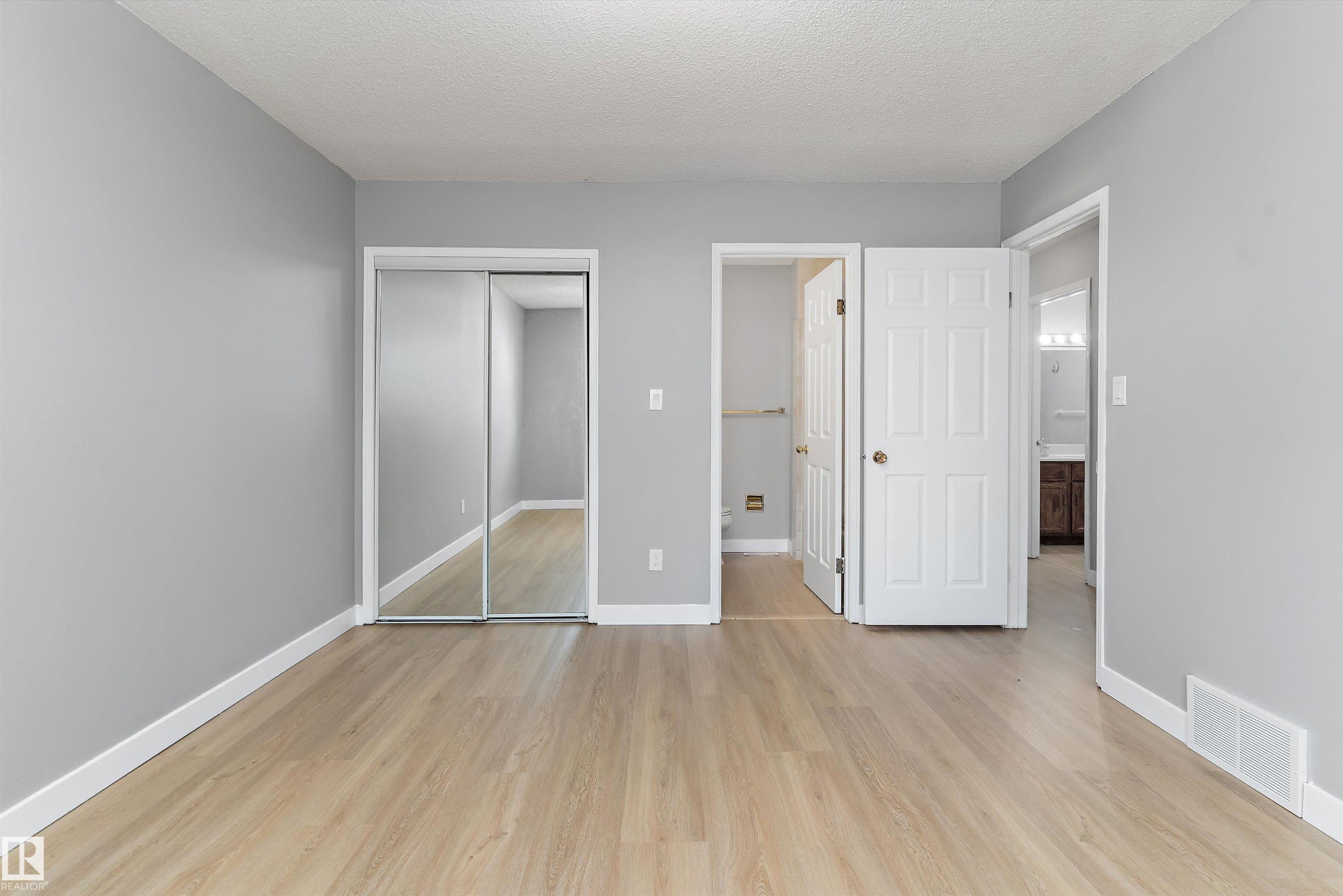 Spacious room featuring light wood-finish flooring, light gray walls, white baseboards, and a white textured ceiling - 14707 33 Street, Edmonton, AB