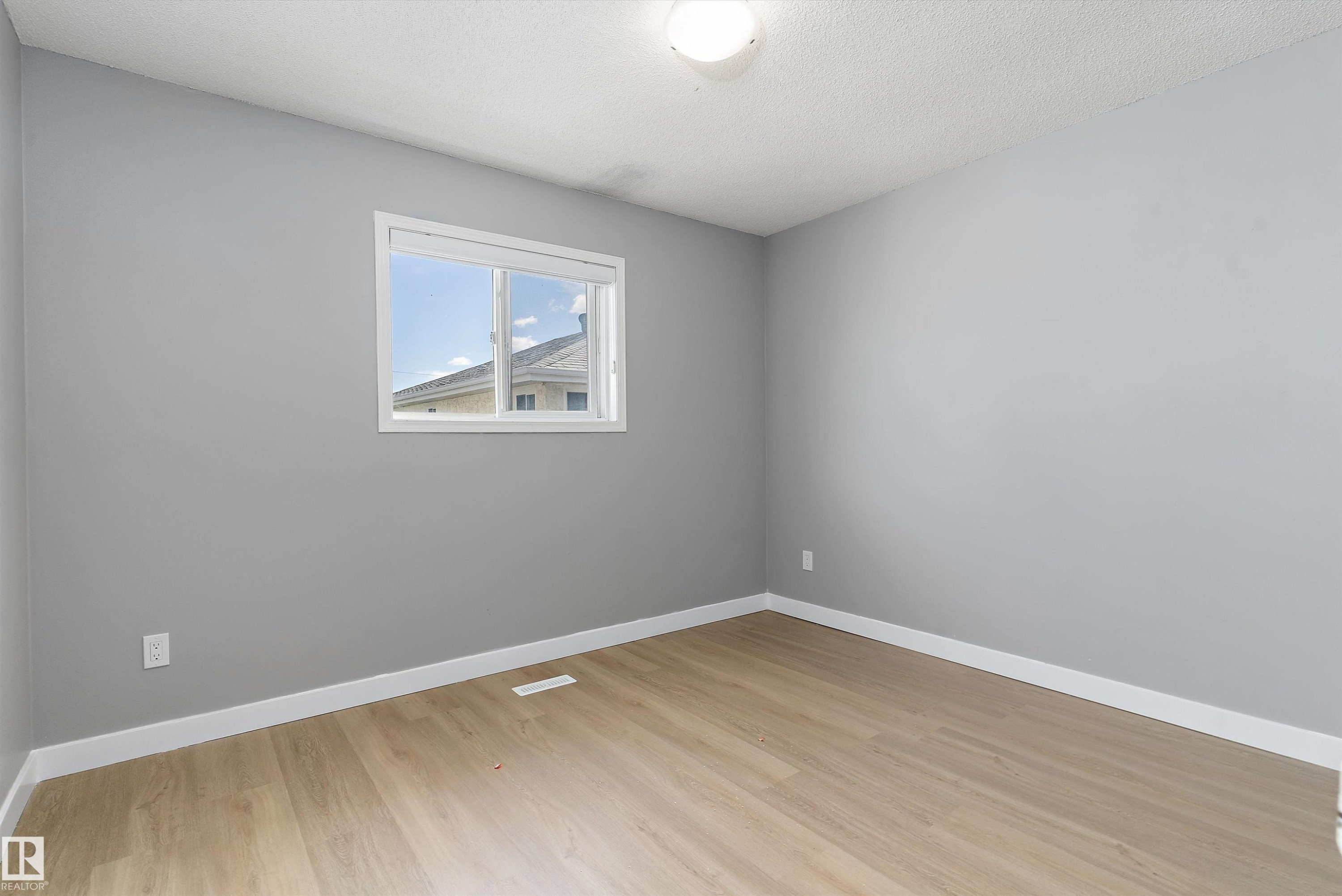 Room featuring neutral gray walls, wood-finish flooring, white baseboards, and a white-framed window - 14707 33 Street, Edmonton, AB