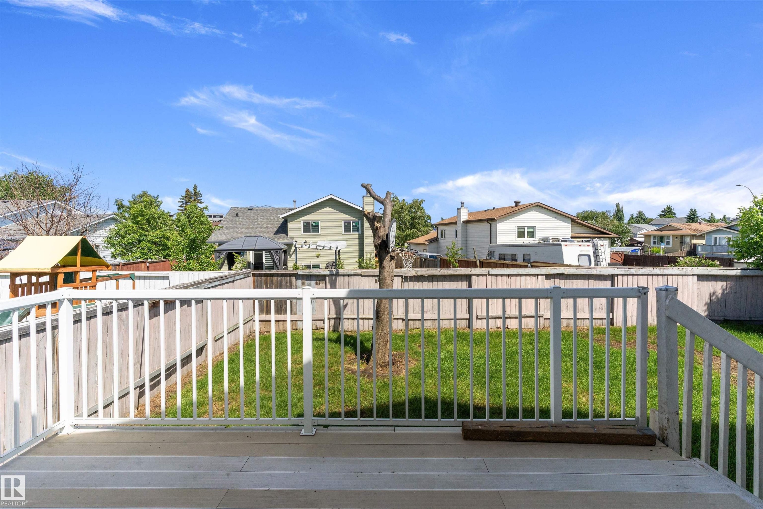 Outdoor deck featuring white railings, a wooden privacy fence, a manicured lawn, and a mature tree - 14707 33 Street, Edmonton, AB