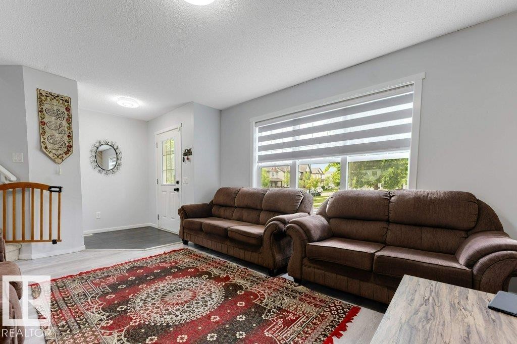 Inviting living space featuring light wood-finish flooring, a prominent window with horizontal blinds, and a white entrance door with decorative glass - 3511 15A Street, Edmonton, AB