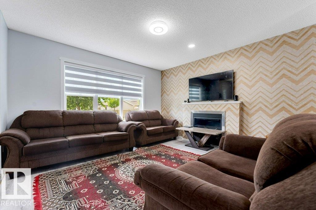 Living room featuring light wood-finish flooring, a contemporary fireplace with a white mantel, and a wall with a chevron pattern - 3511 15A Street, Edmonton, AB