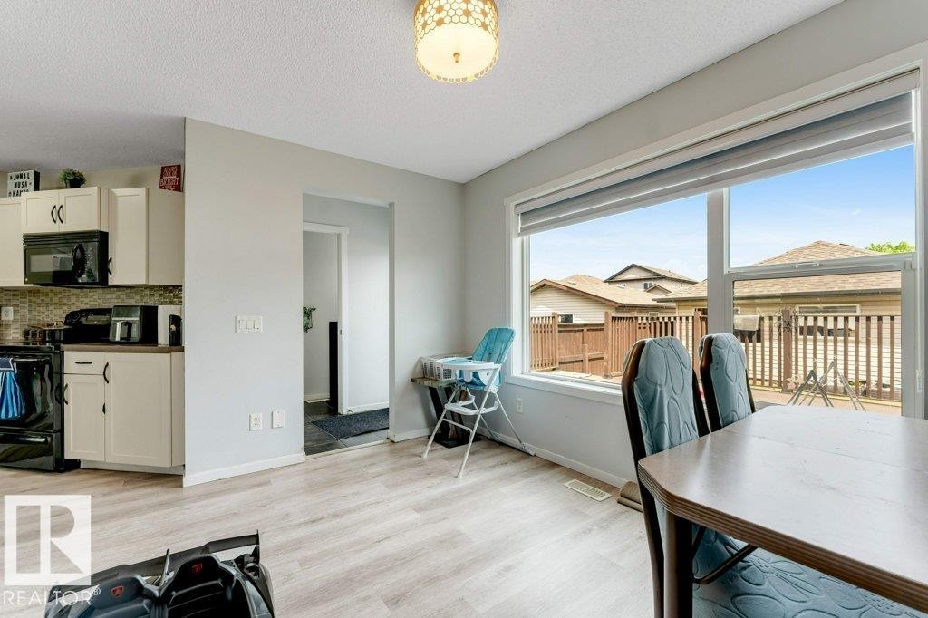 Open-concept dining area featuring light wood-finish flooring, a contemporary ceiling light fixture, a large picture window, and direct access to the kitchen area - 3511 15A Street, Edmonton, AB