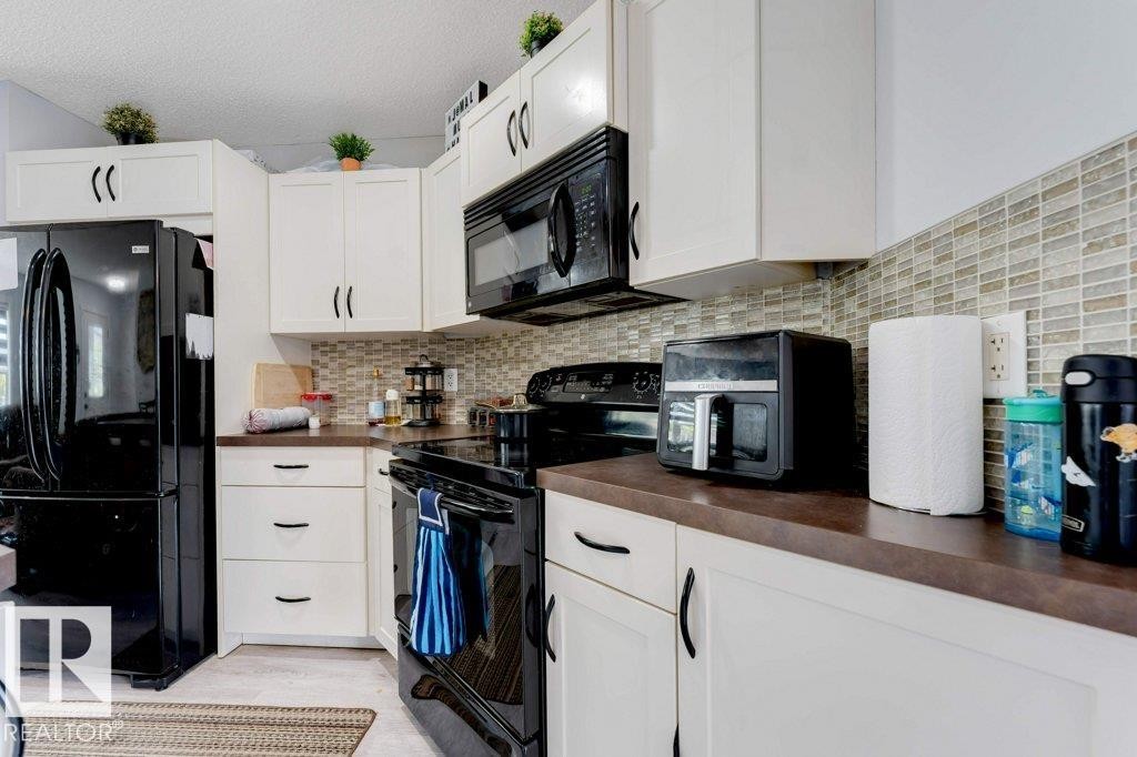 Kitchen featuring white cabinetry with dark hardware, dark countertops, and a full tile backsplash - 3511 15A Street, Edmonton, AB