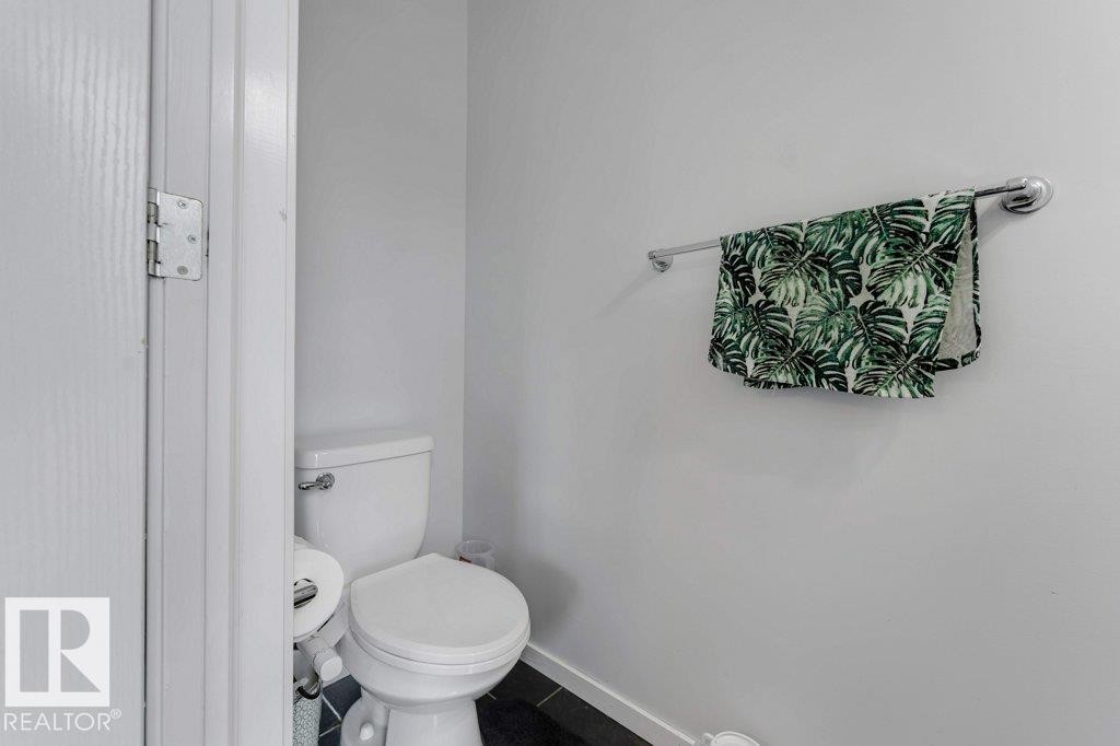 Compact powder room featuring a white toilet, black tile flooring, light-toned walls, and a chrome towel bar - 3511 15A Street, Edmonton, AB