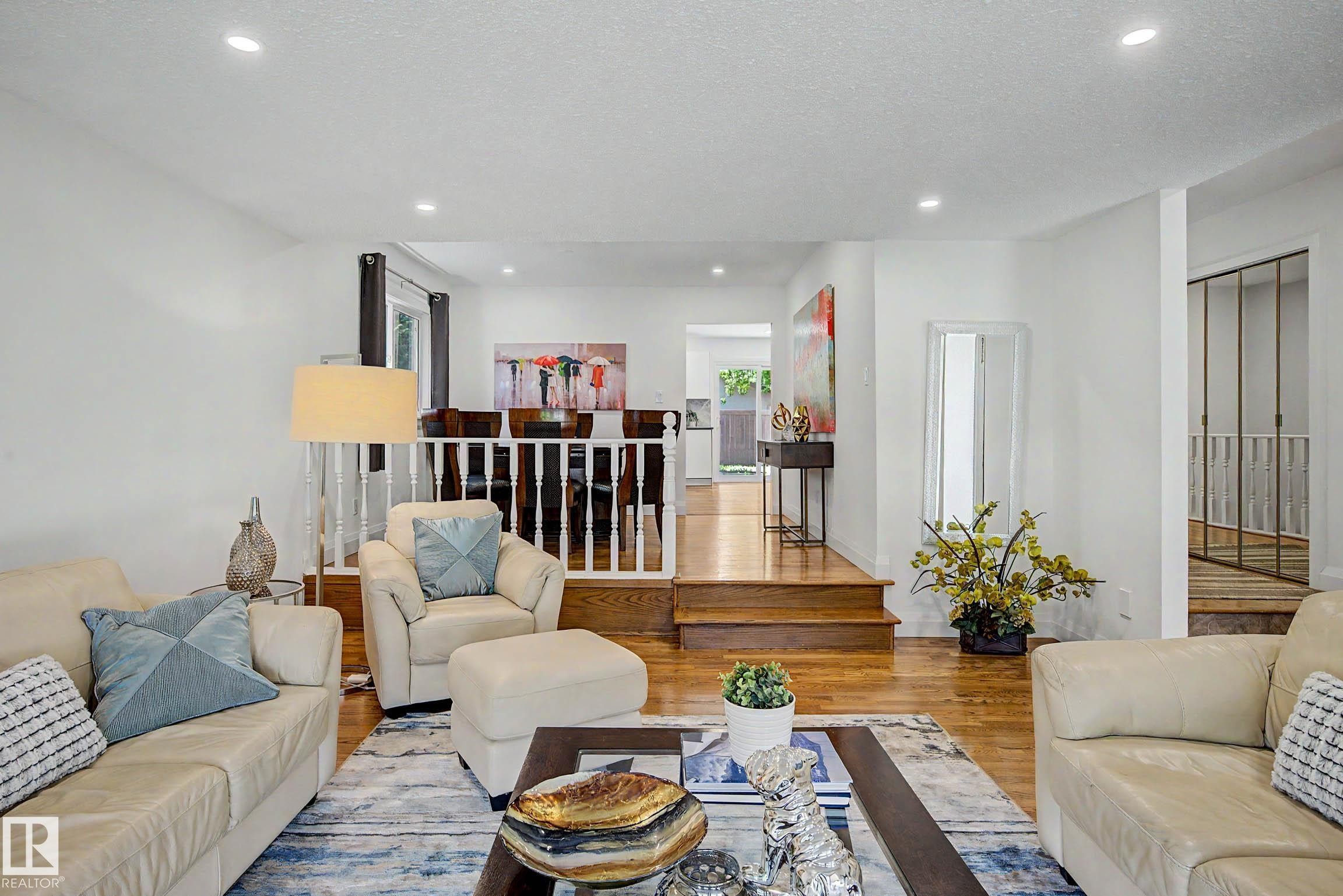 Spacious living area featuring wood-finish flooring, recessed lighting, and a white baluster railing - 3718 103B Street Nw, Edmonton, AB - Indoor Photo Showing Living Room