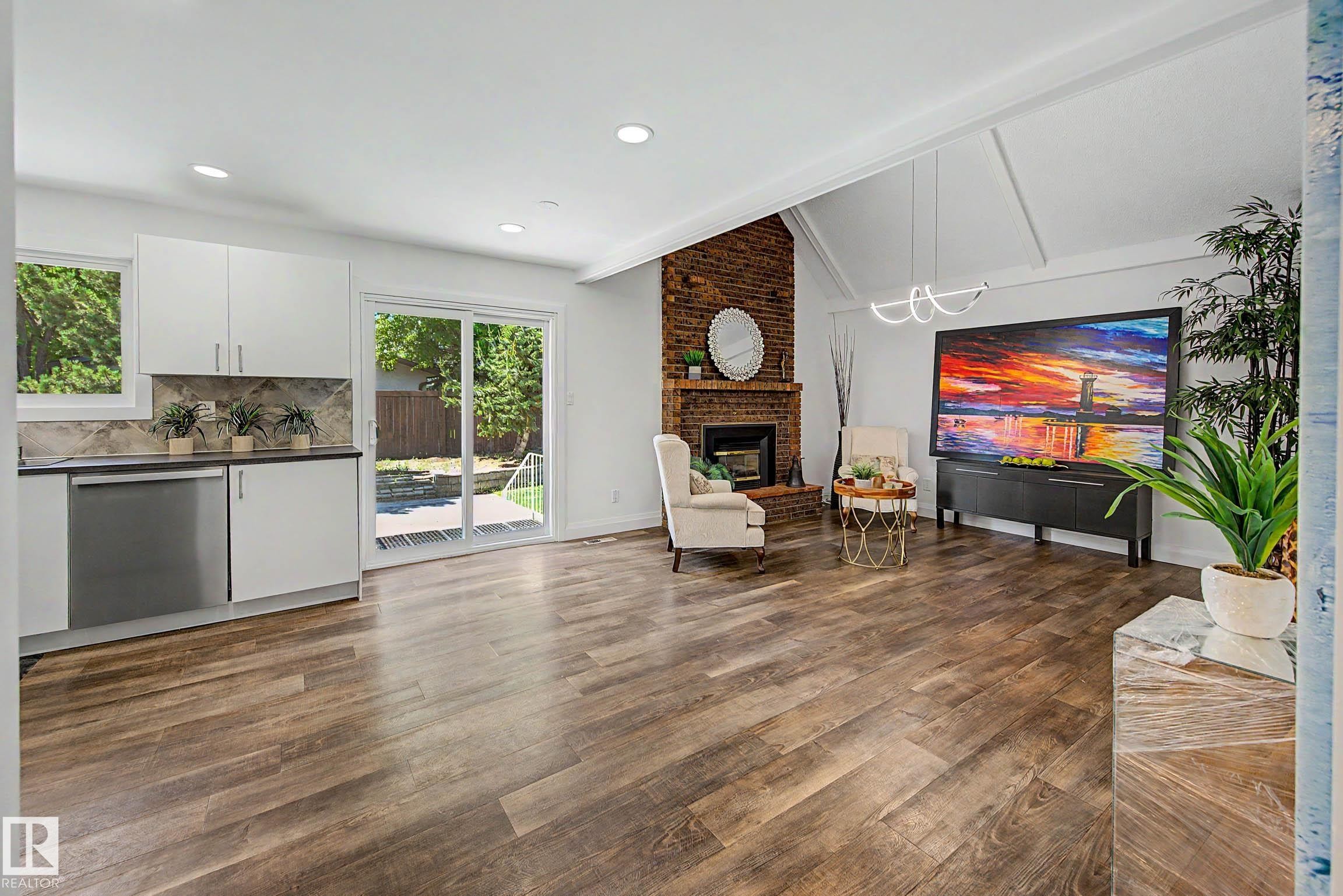Open-concept living space featuring wood-finish flooring, a brick-surround fireplace, and vaulted ceilings with exposed beams - 3718 103B Street Nw, Edmonton, AB - Indoor With Fireplace
