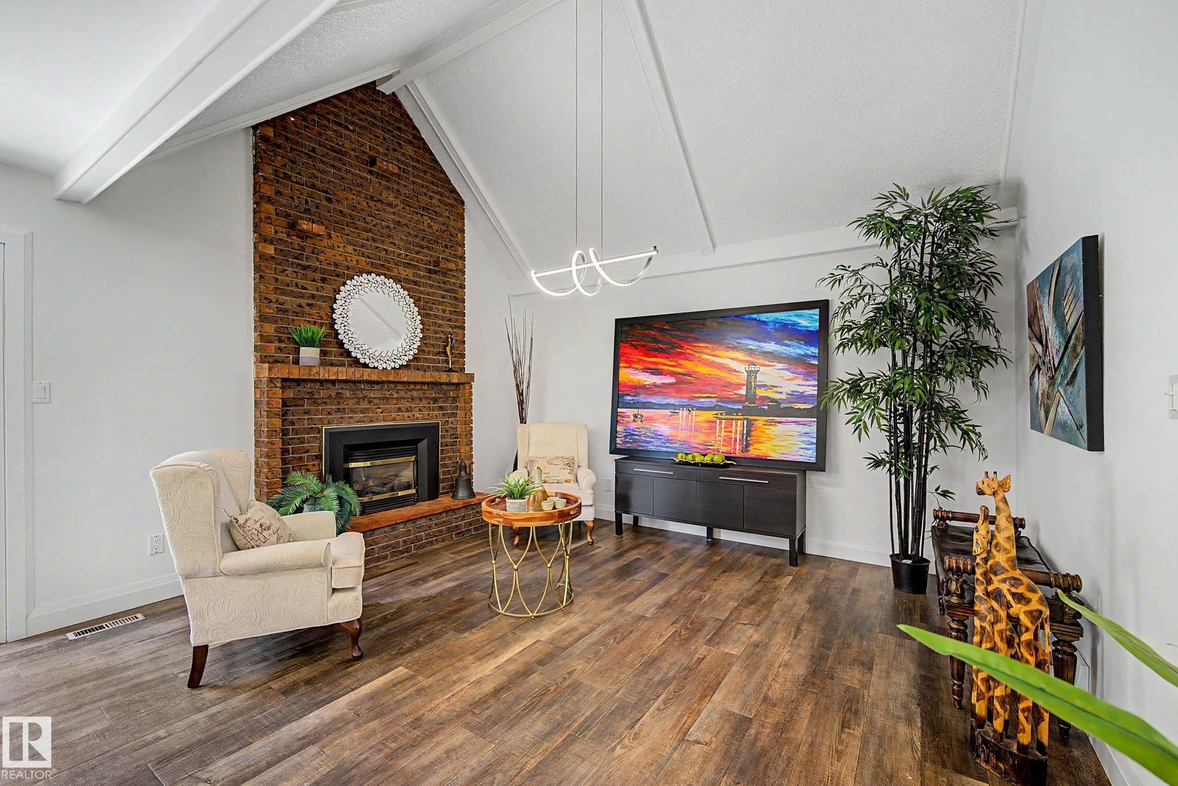 Vaulted ceiling with exposed beams, brick fireplace, wood-finish flooring, and modern lighting fixture - 3718 103B Street Nw, Edmonton, AB - Indoor With Fireplace