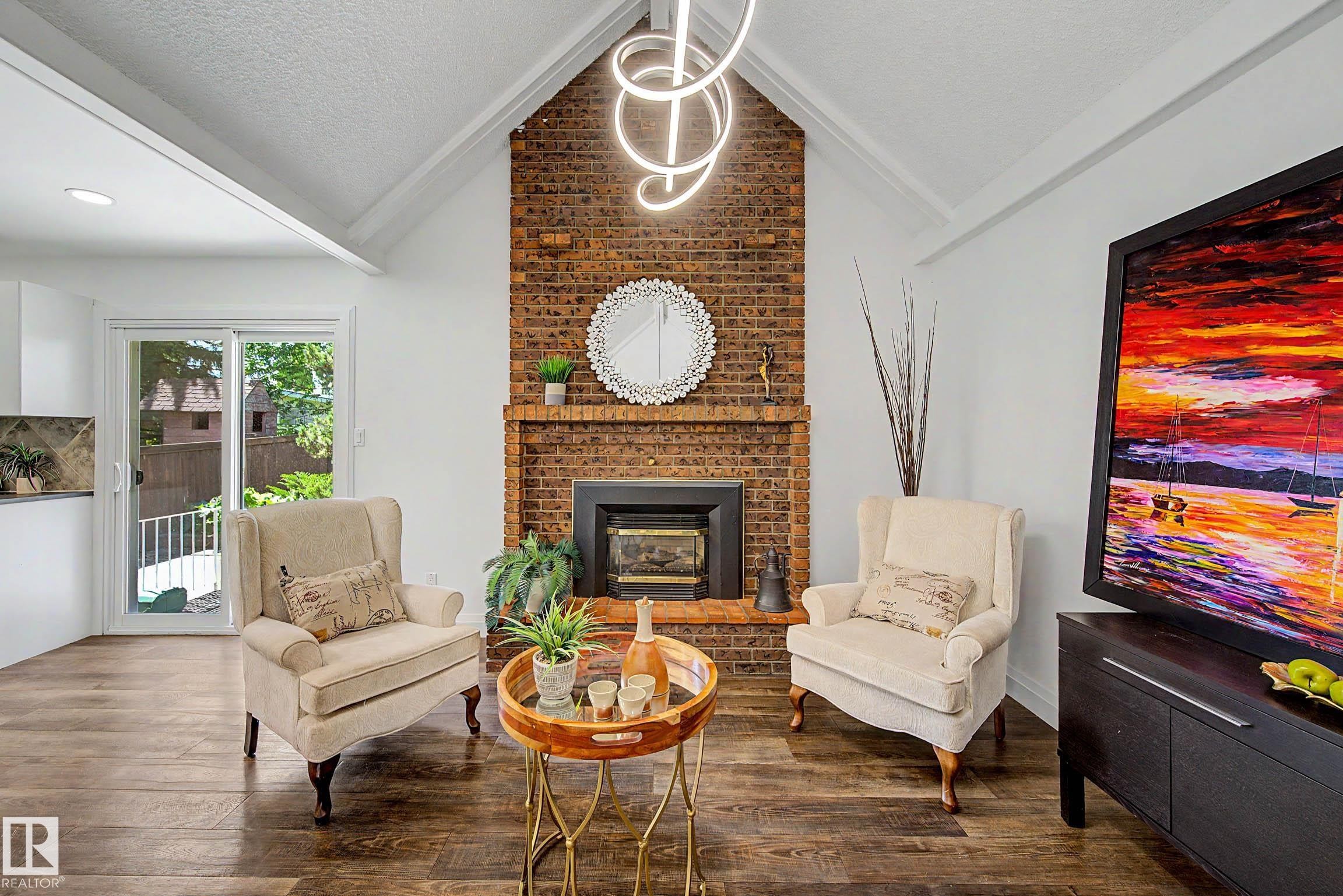 Vaulted ceilings with a unique linear light fixture, brick-clad fireplace with wood mantle, wood-finish flooring, and sliding glass doors to the exterior - 3718 103B Street Nw, Edmonton, AB - Indoor Photo Showing Living Room With Fireplace
