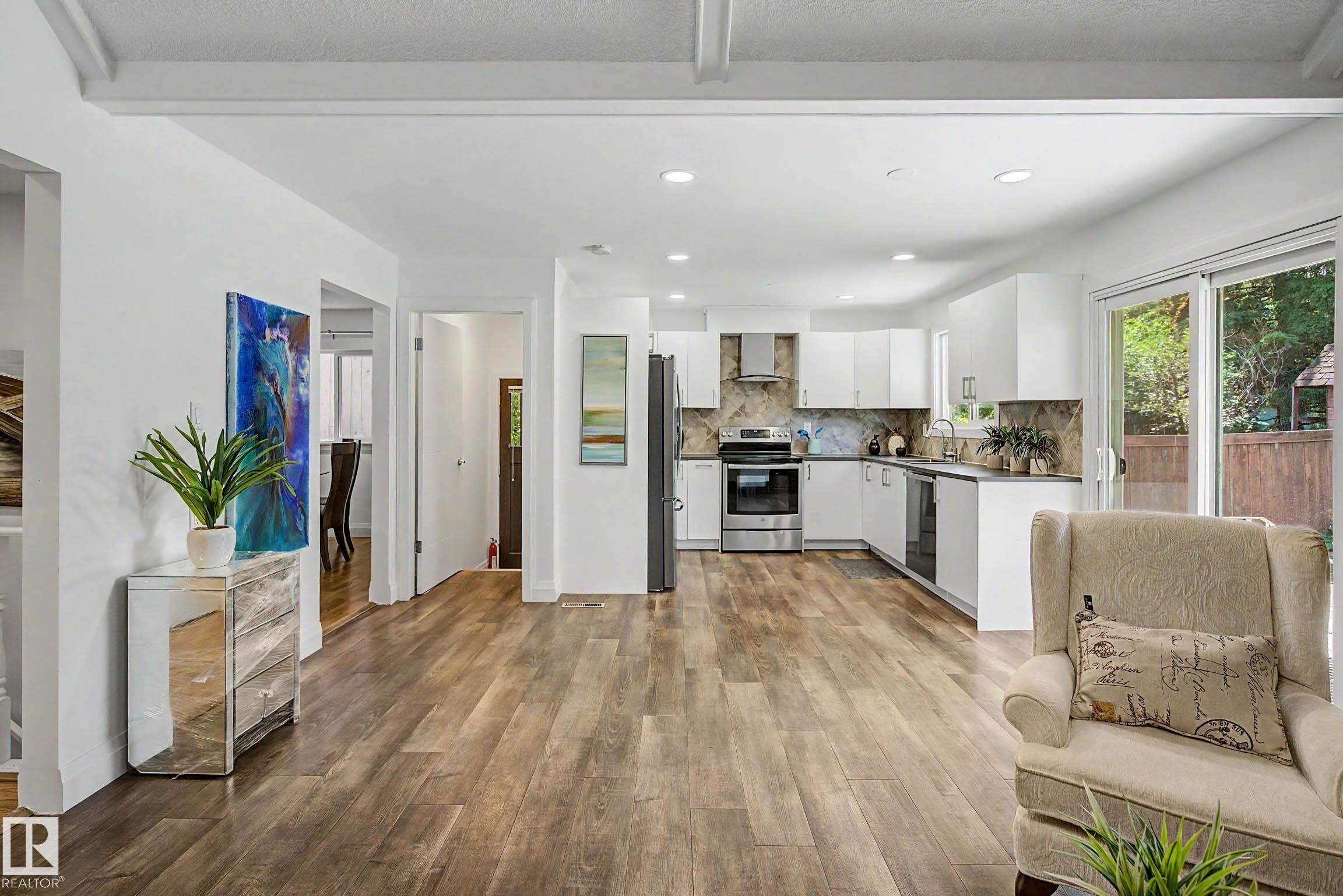 Open-concept living area featuring wood-finish flooring, recessed lighting, and a kitchen with white cabinetry, stainless steel appliances, and a tiled backsplash - 3718 103B Street Nw, Edmonton, AB - Indoor Photo Showing Kitchen