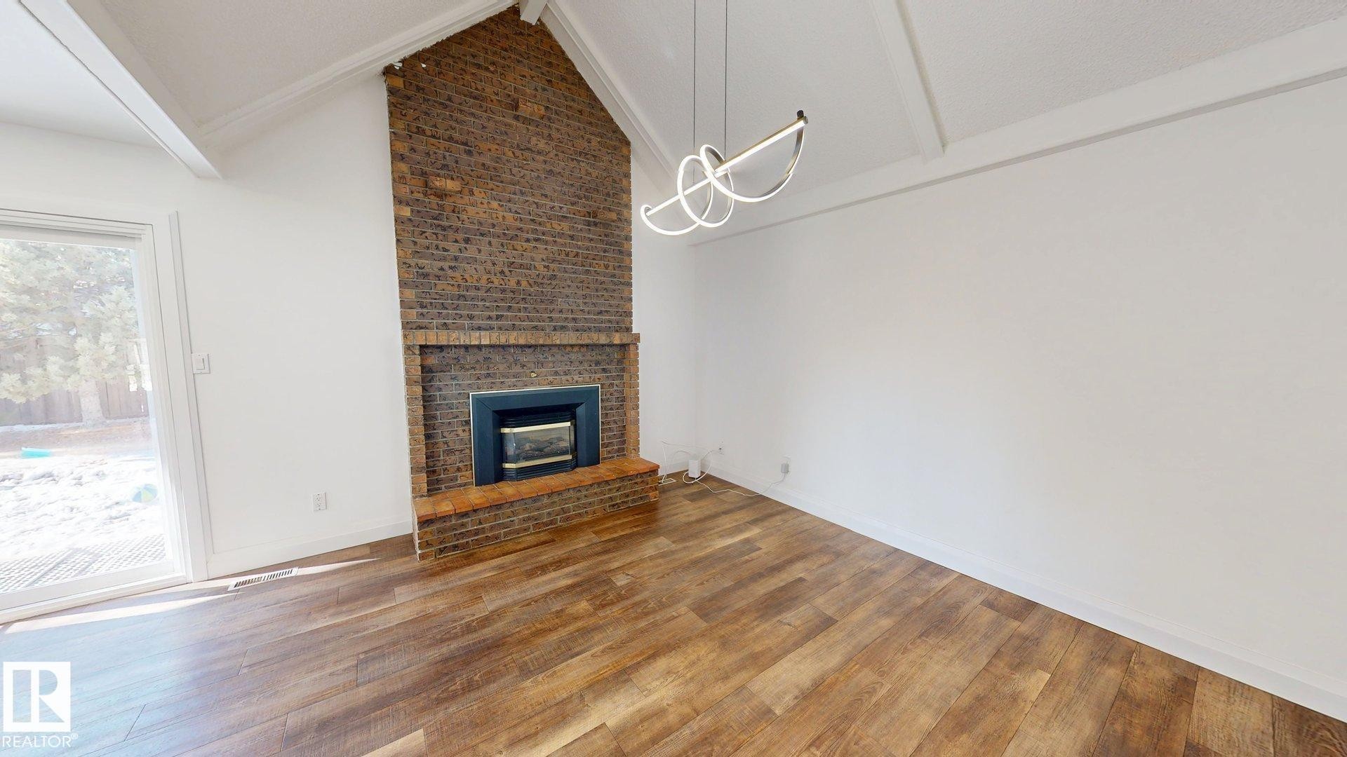 Vaulted ceilings with exposed beams and a contemporary light fixture complement the brick fireplace with hearth - 3718 103B Street, Edmonton, AB
