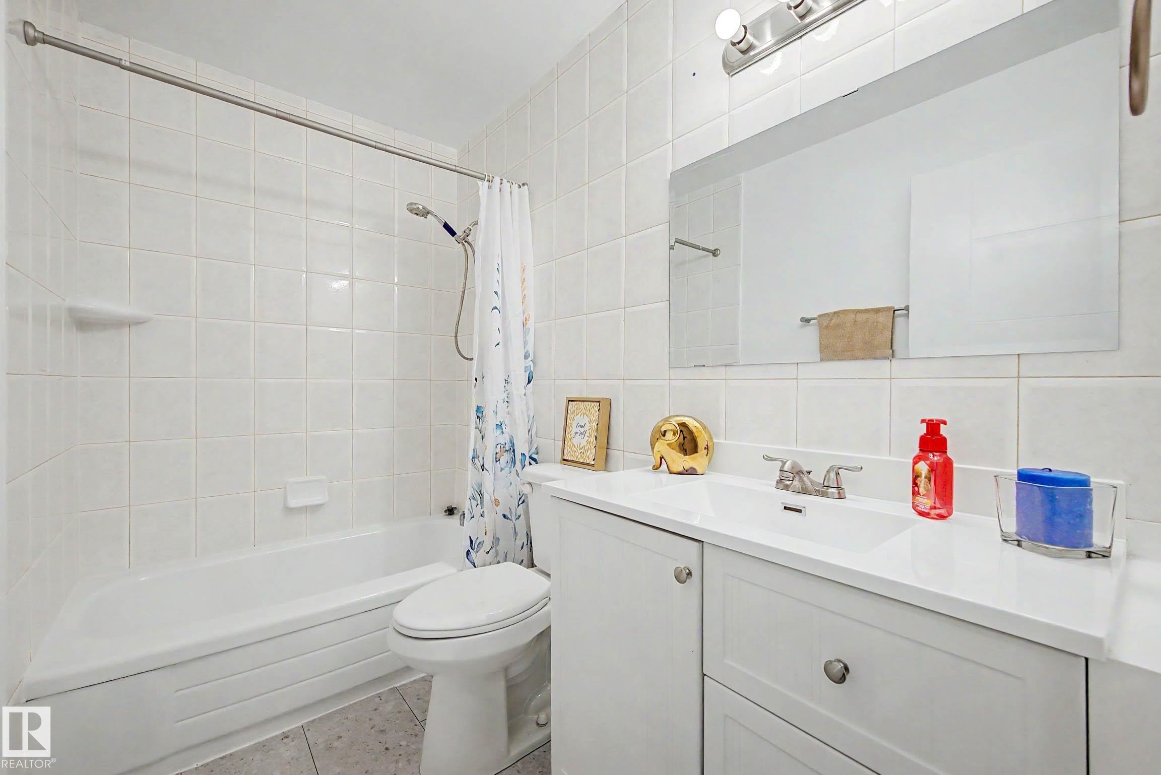Full bathroom featuring a white porcelain tub with shower, white square wall tiling, and a vanity with an integrated sink and base cabinetry - 3718 103B Street Nw, Edmonton, AB - Indoor Photo Showing Bathroom