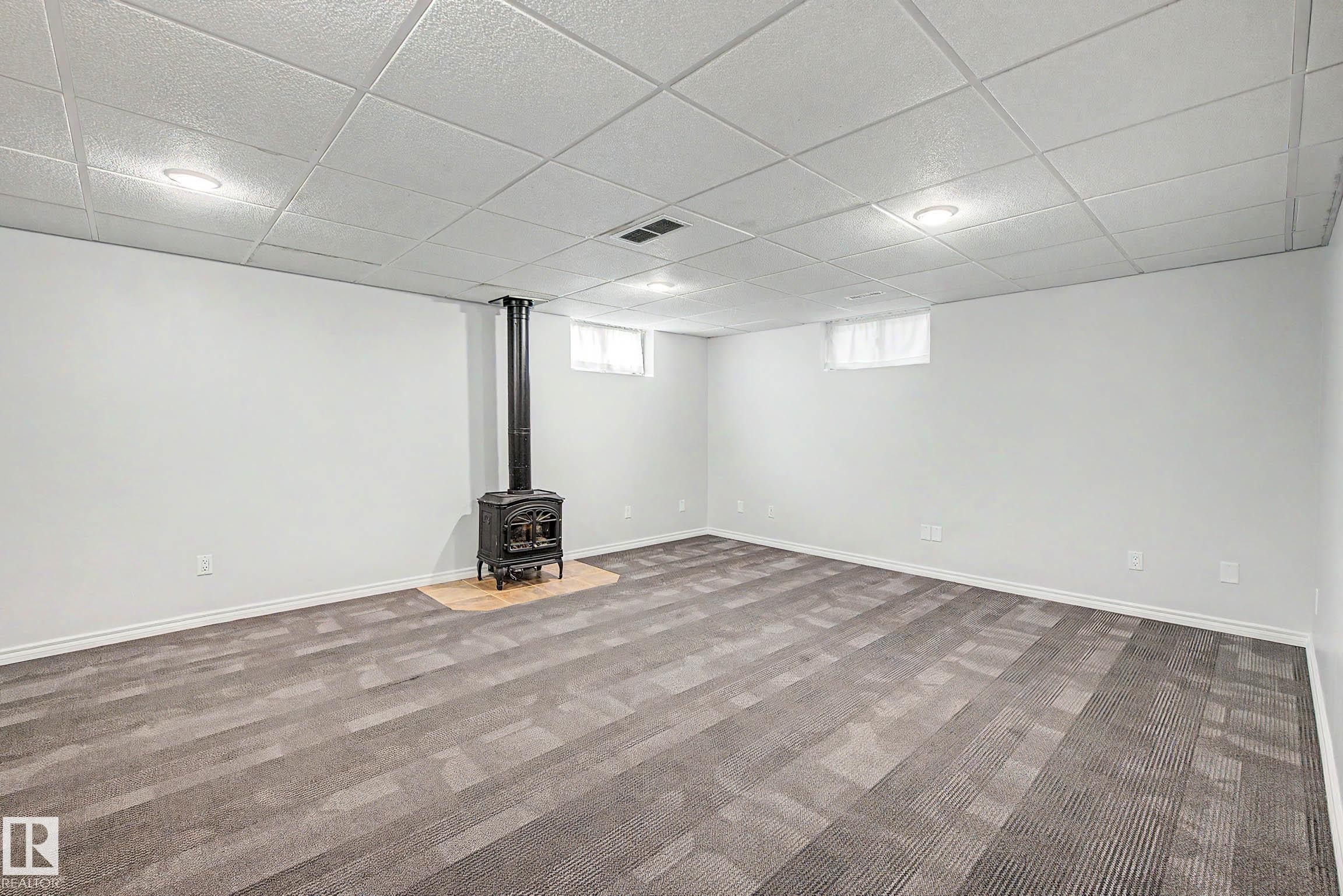 Spacious room featuring a central wood-burning stove with a light-toned hearth - 3718 103B Street Nw, Edmonton, AB - Indoor