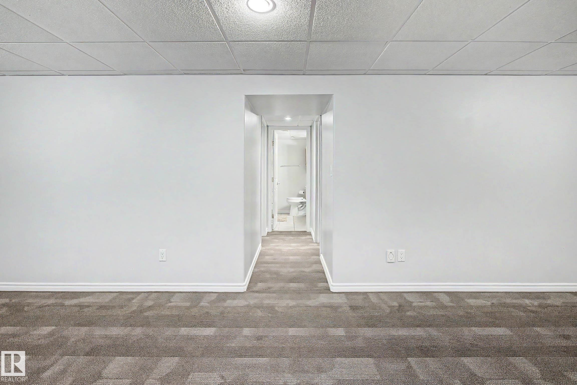 Spacious room featuring neutral carpeting with a geometric pattern, crisp white walls, and a suspended acoustic tile ceiling with recessed lighting - 3718 103B Street Nw, Edmonton, AB - Indoor Photo Showing Other Room