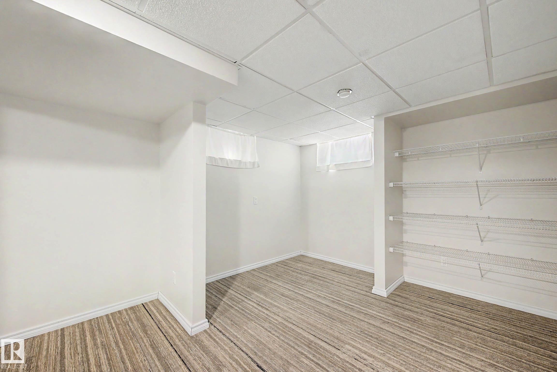 Spacious room featuring wood-finish flooring, white walls, and a drop ceiling with recessed lighting - 3718 103B Street Nw, Edmonton, AB - Indoor