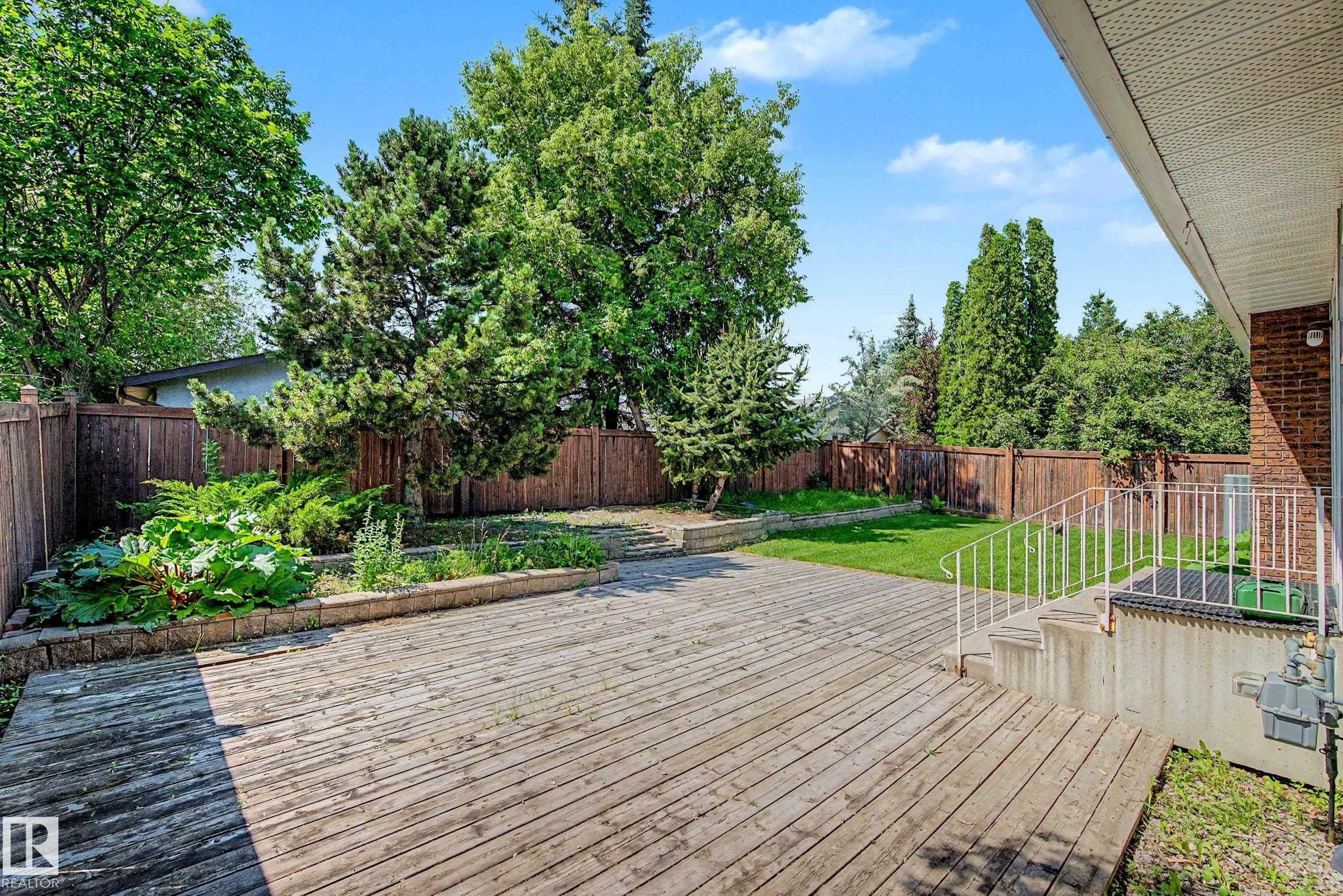 Expansive wooden deck with a built-in planter, surrounded by mature trees and a privacy fence - 3718 103B Street Nw, Edmonton, AB - Outdoor