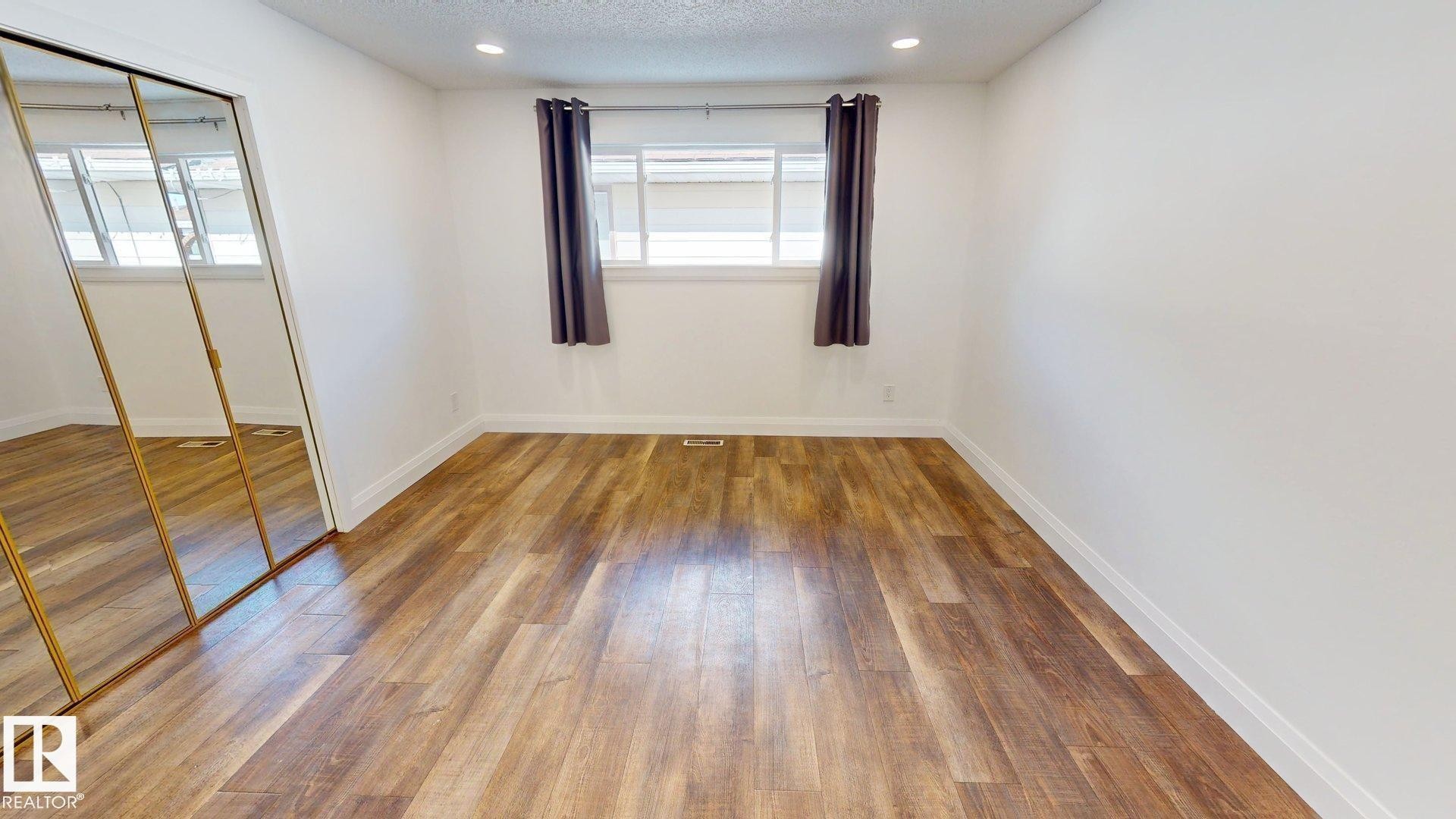 Bright room featuring wood-finish flooring, white walls, and a mirrored sliding closet door - 3718 103B Street, Edmonton, AB