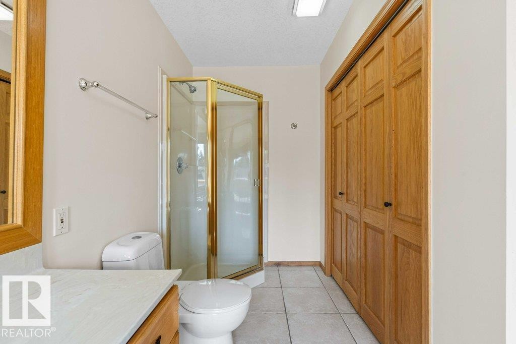 Bathroom featuring vanity, a stall shower, light tile patterned floors, a textured ceiling, and a closet - 738 Wheeler Road, Edmonton, AB