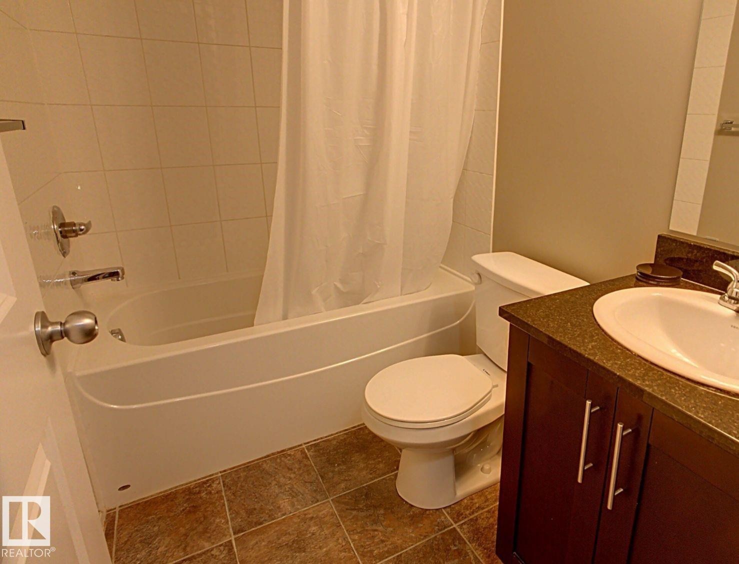Bathroom featuring a shower-tub combination with white tile surround, a dark wood-finish vanity with a light-colored countertop, and a white basin sink with chrome fixtures - 328 3315 James Mowatt Trail, Edmonton, AB