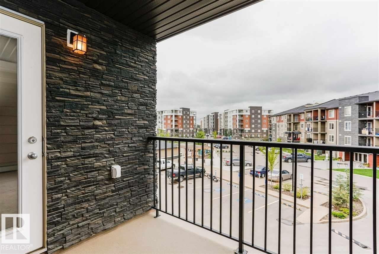 Balcony featuring a dark stacked stone accent wall, exterior wall sconce, and black metal railing - 328 3315 James Mowatt Trail, Edmonton, AB