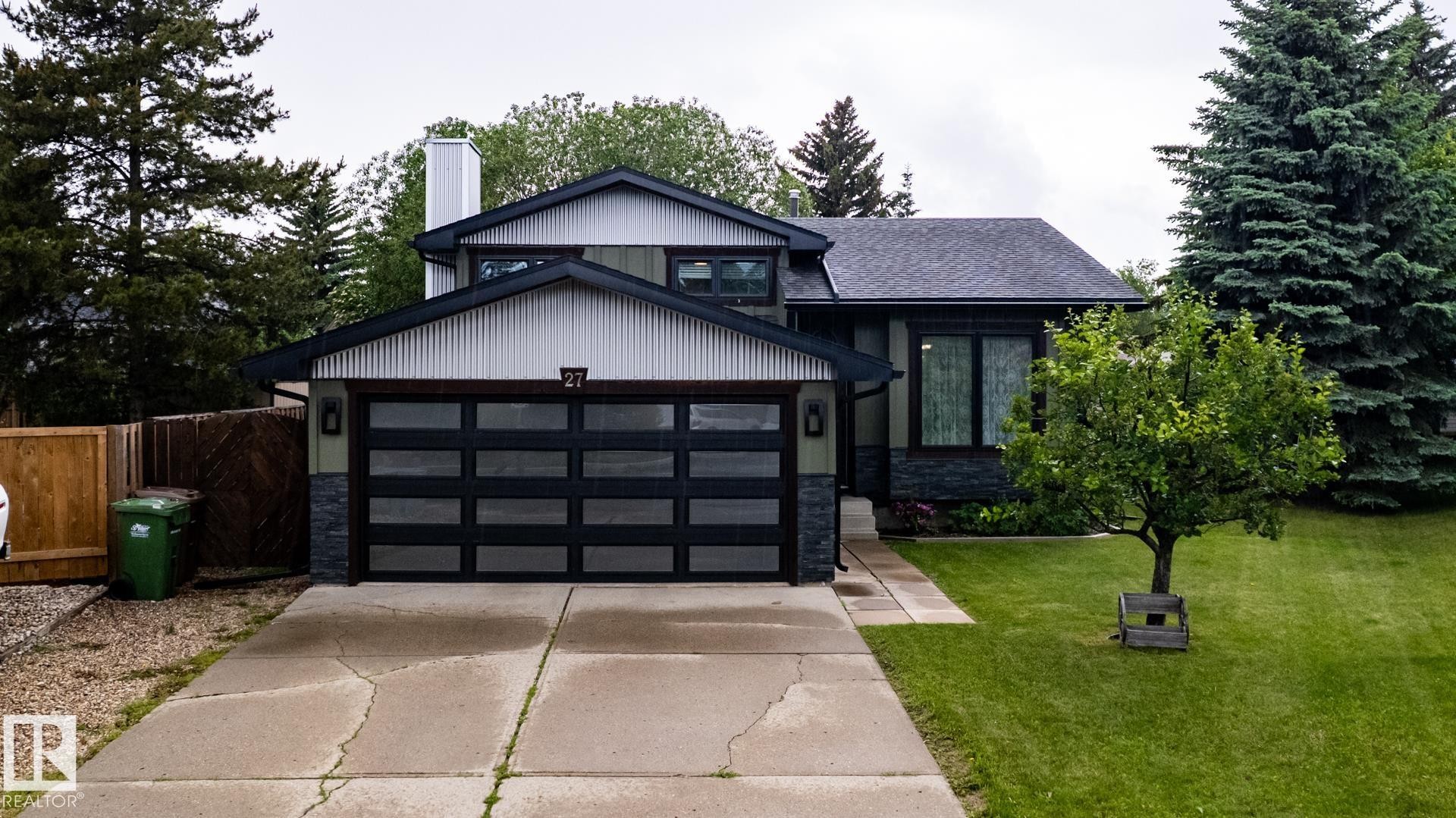 Modern dwelling featuring a black paneled garage door, dark stone veneer accents, and a complementary gray siding - 27 Danforth Crescent, St. Albert, AB