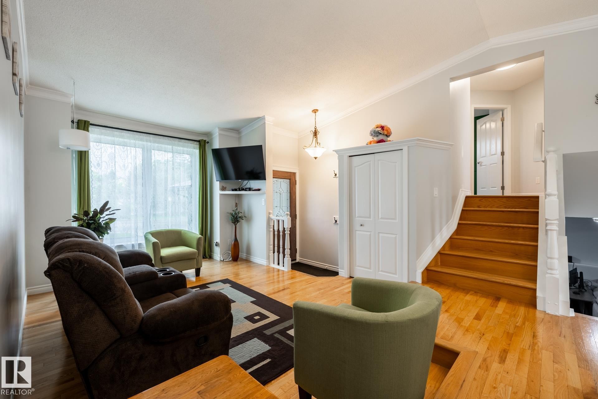 Hardwood flooring throughout the main living area, featuring a prominent window, a built-in closet, and a staircase with white balusters - 27 Danforth Crescent, St. Albert, AB