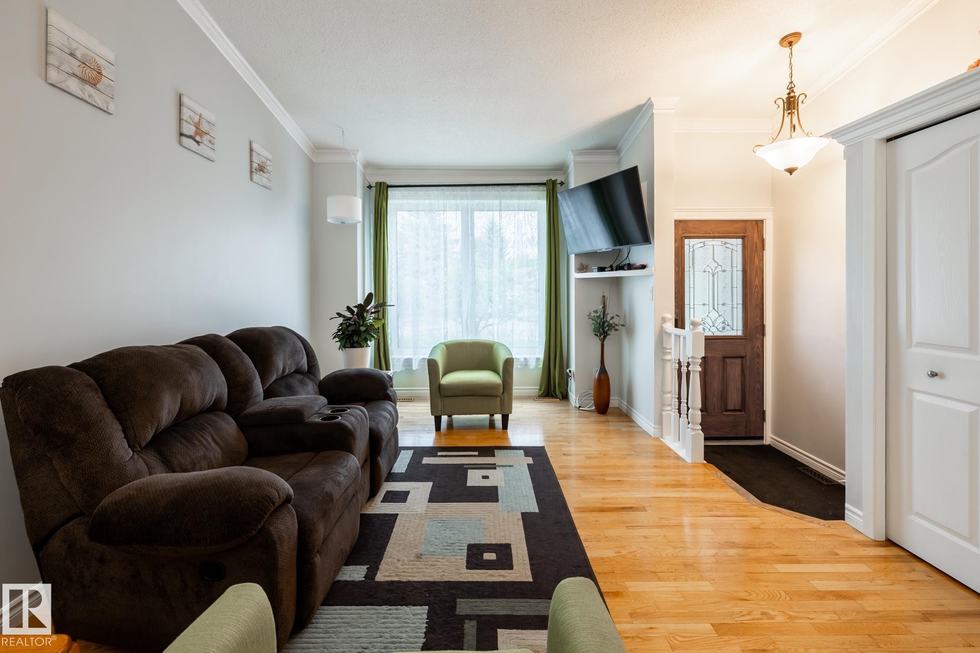 Bright living area featuring wood-finish flooring, white crown molding, and a decorative front entry door with privacy glass - 27 Danforth Crescent, St. Albert, AB