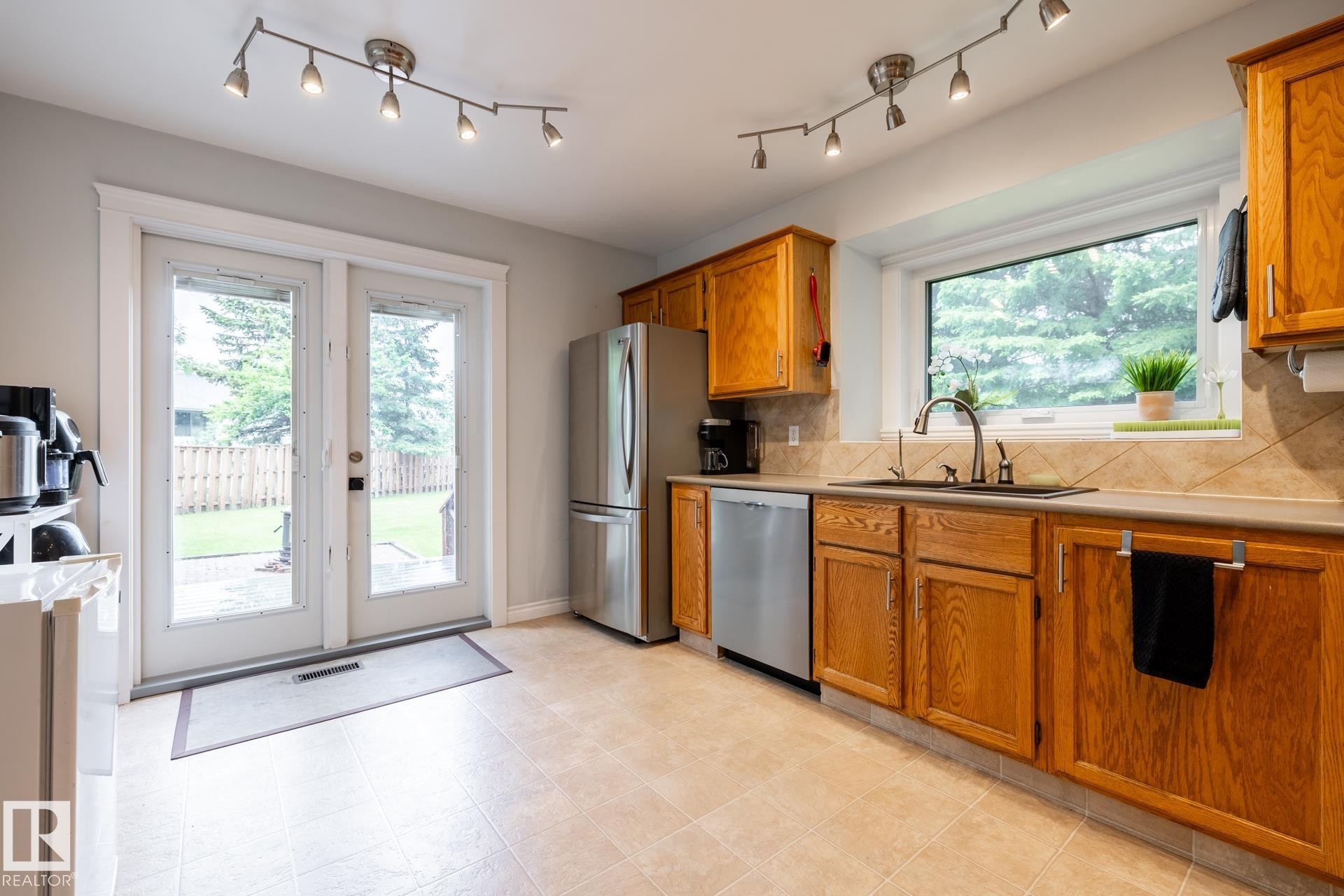 Kitchen featuring wood cabinetry, stainless steel appliances, a tile backsplash, and track lighting - 27 Danforth Crescent, St. Albert, AB
