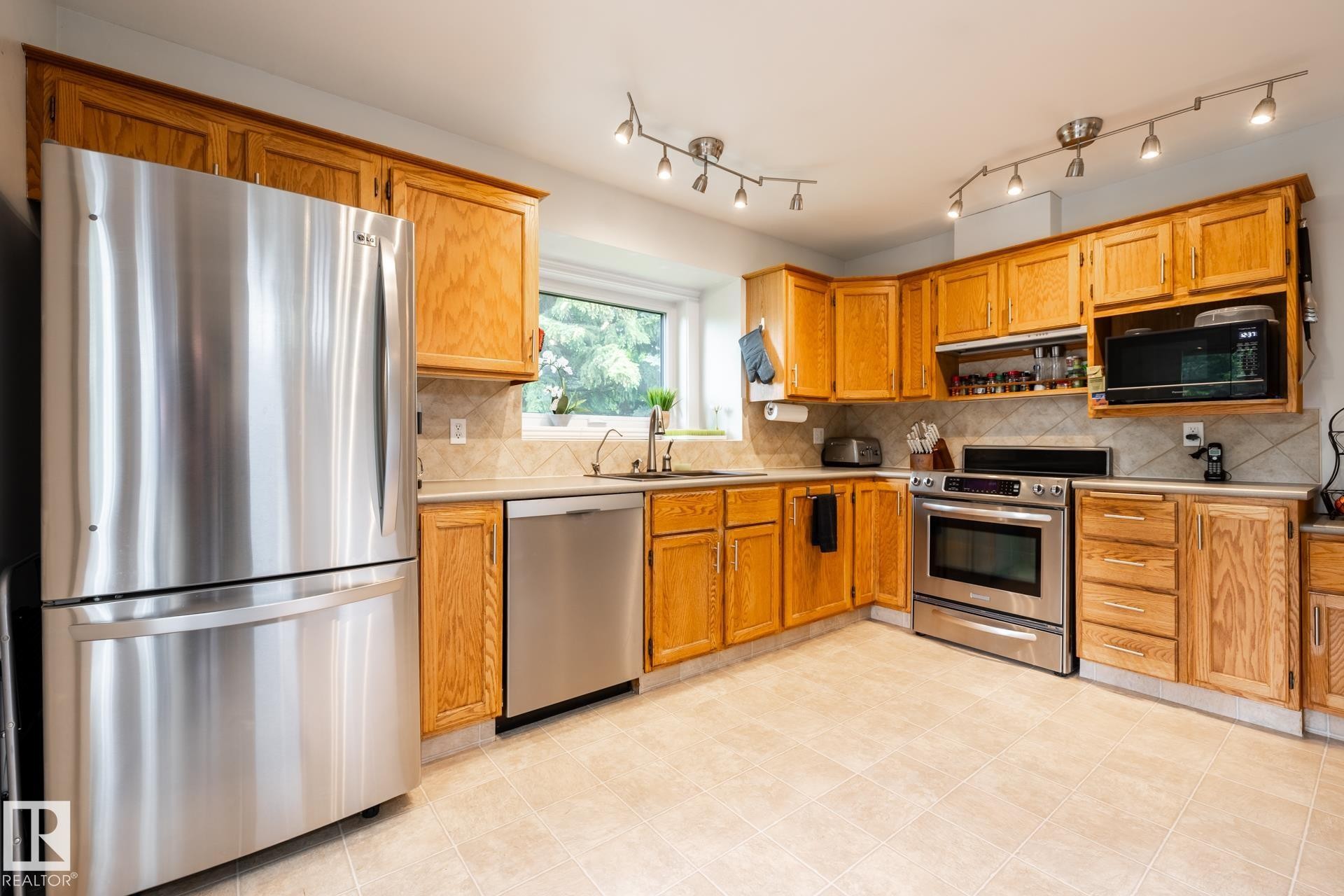 Kitchen featuring light wood cabinetry, stainless steel appliances, and a tiled backsplash - 27 Danforth Crescent, St. Albert, AB