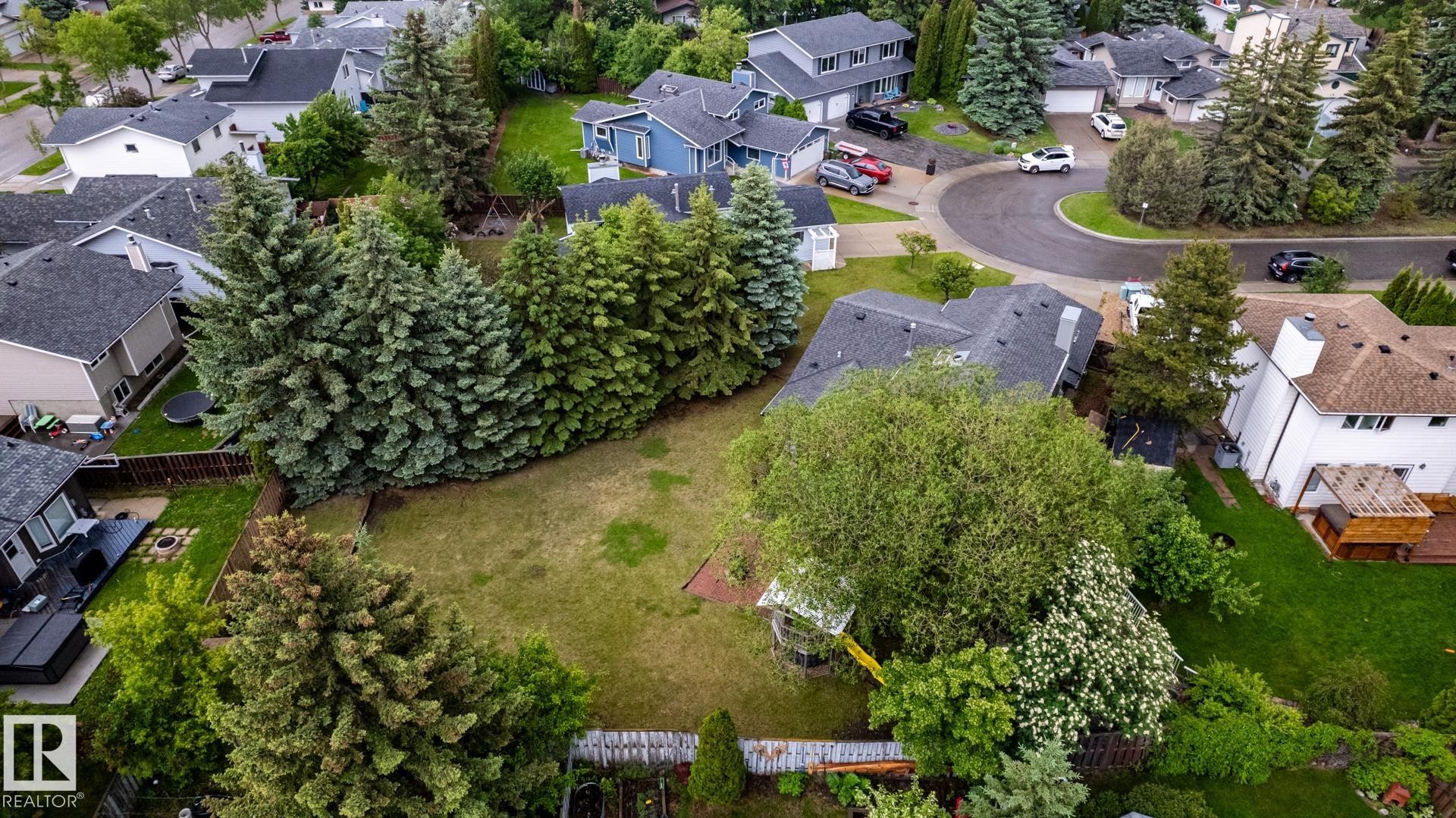 Expansive grassy backyard featuring a fenced perimeter and mature trees - 27 Danforth Crescent, St. Albert, AB