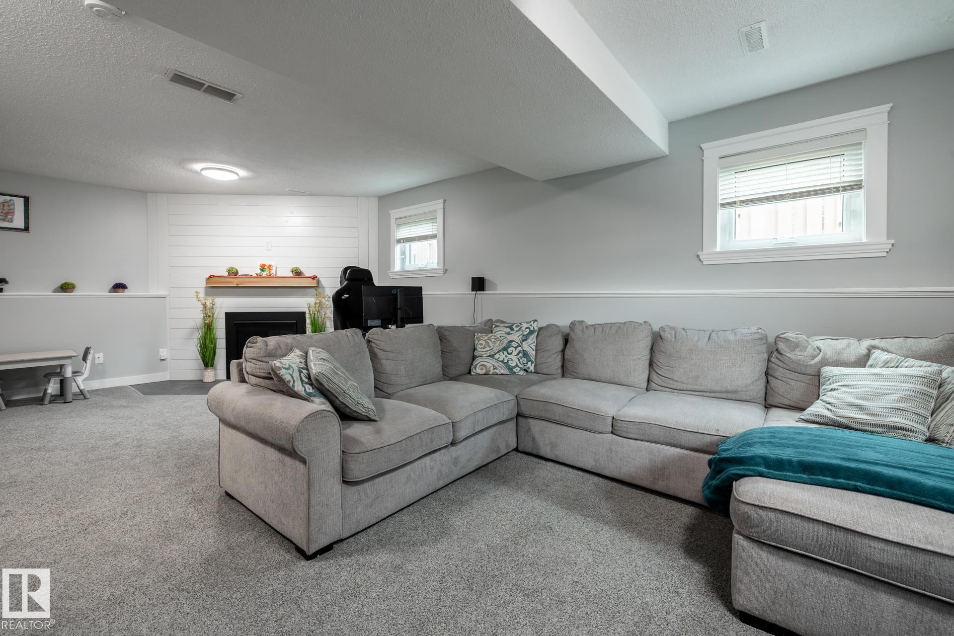 Carpeted lower level featuring a fireplace with a wood mantel and shiplap-style wall, built-in recessed lighting, and a chair rail - 27 Danforth Crescent, St. Albert, AB