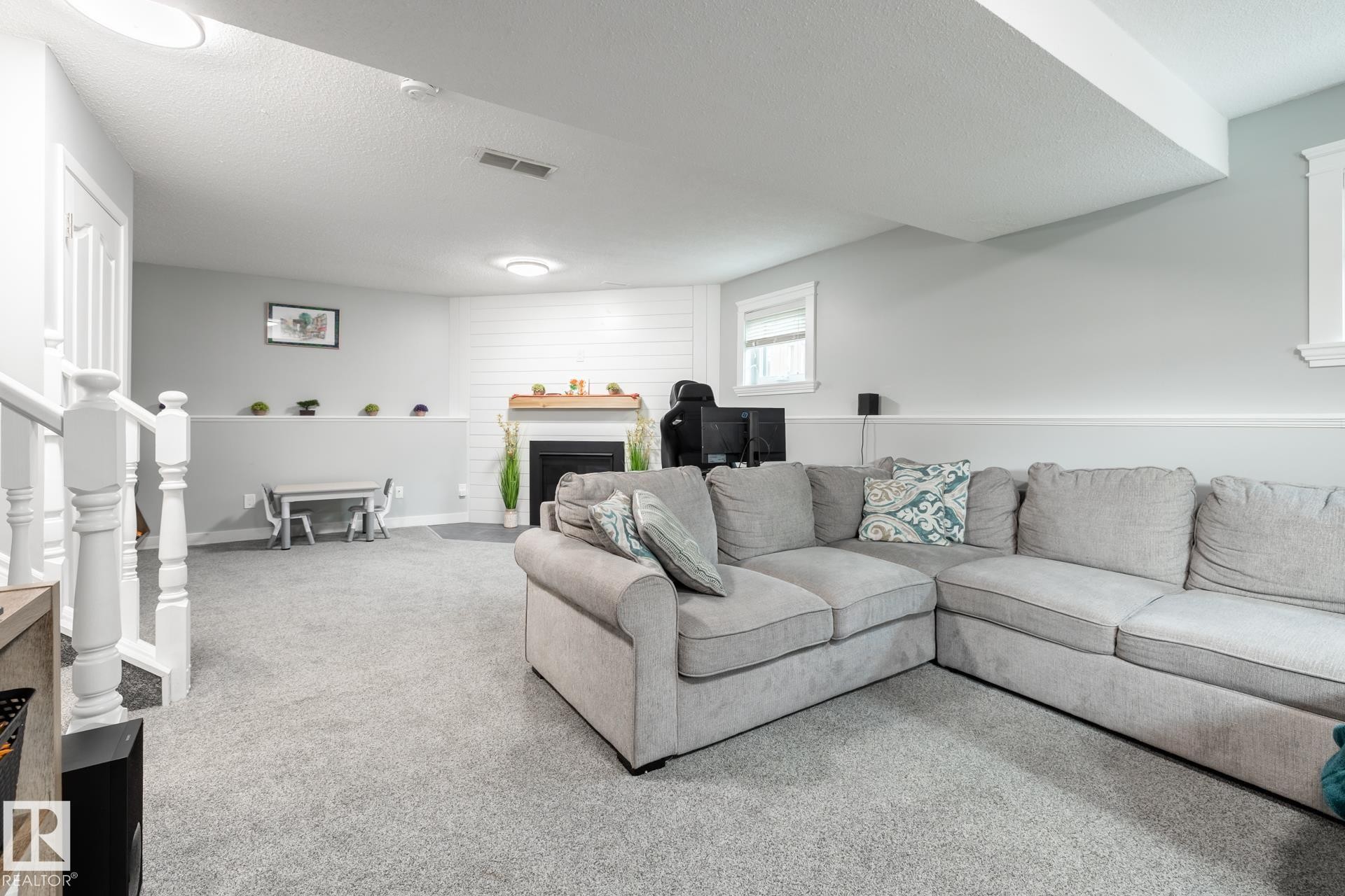 Spacious lower-level area featuring a fireplace with a wood-finish mantel and shiplap-style surround - 27 Danforth Crescent, St. Albert, AB