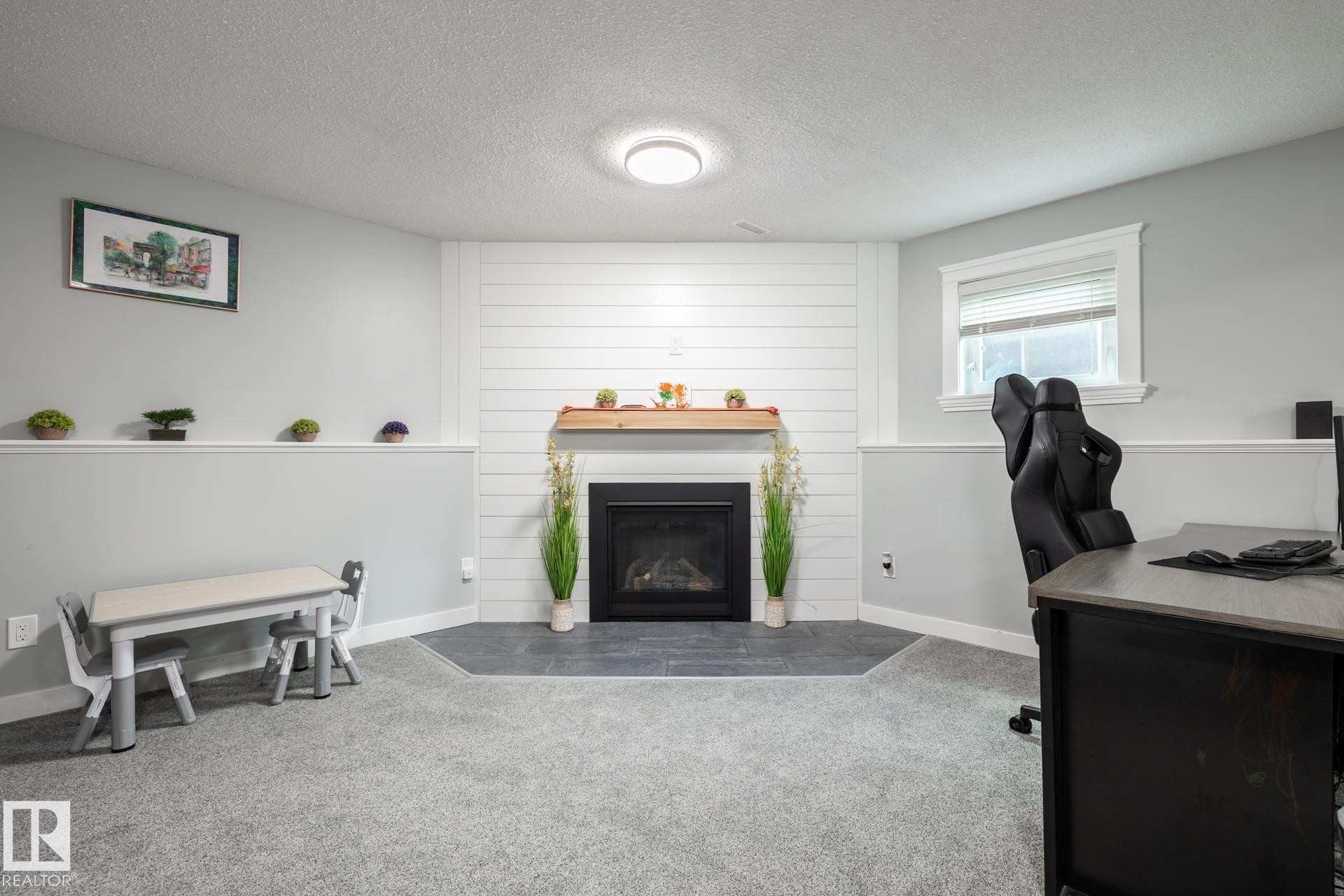 Carpeted room featuring a fireplace with a wood mantle and shiplap surround, a single window, and a built-in shelf with trim - 27 Danforth Crescent, St. Albert, AB