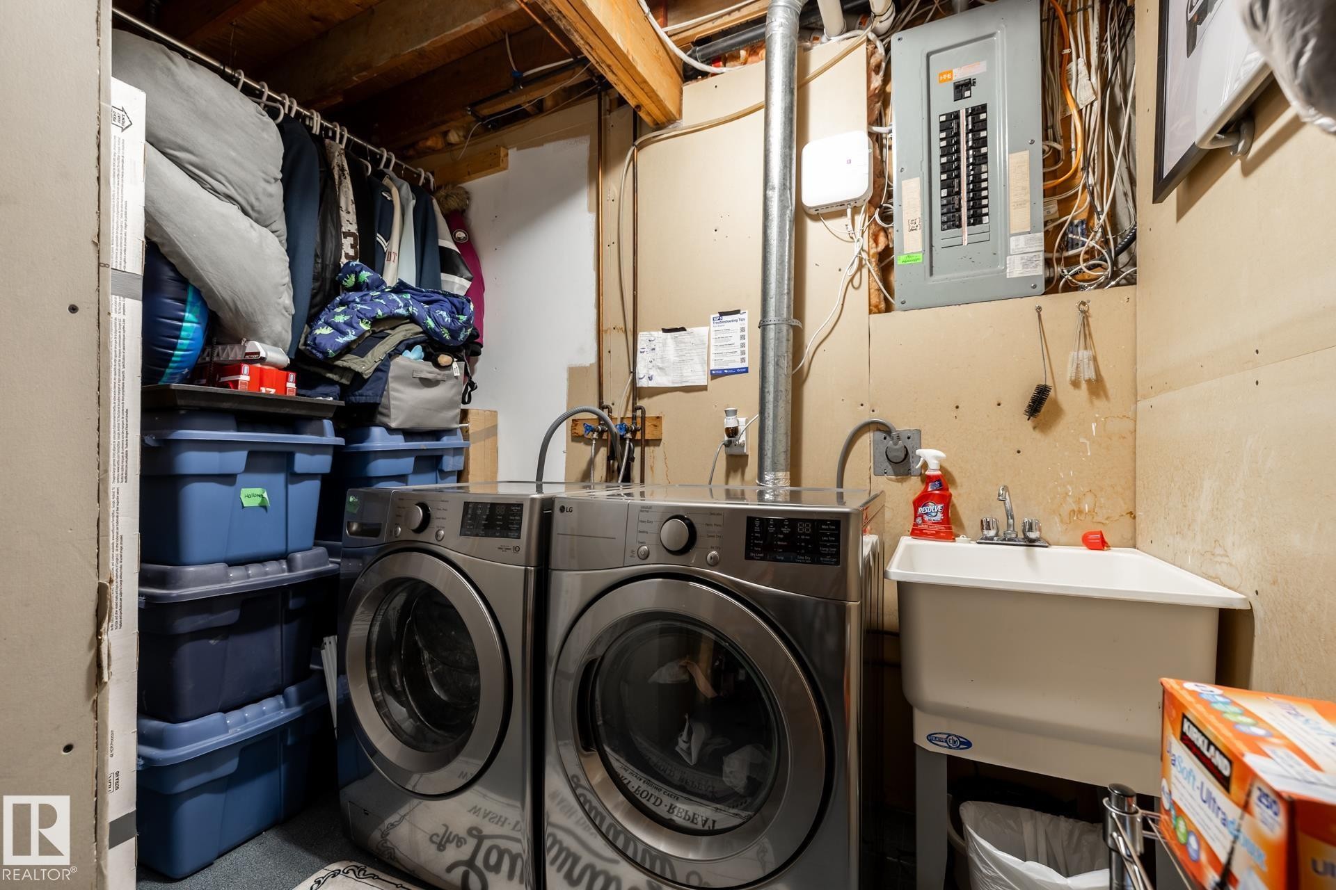Dedicated utility area featuring a wall-mounted electrical panel, exposed ceiling joists, and a utility sink - 27 Danforth Crescent, St. Albert, AB