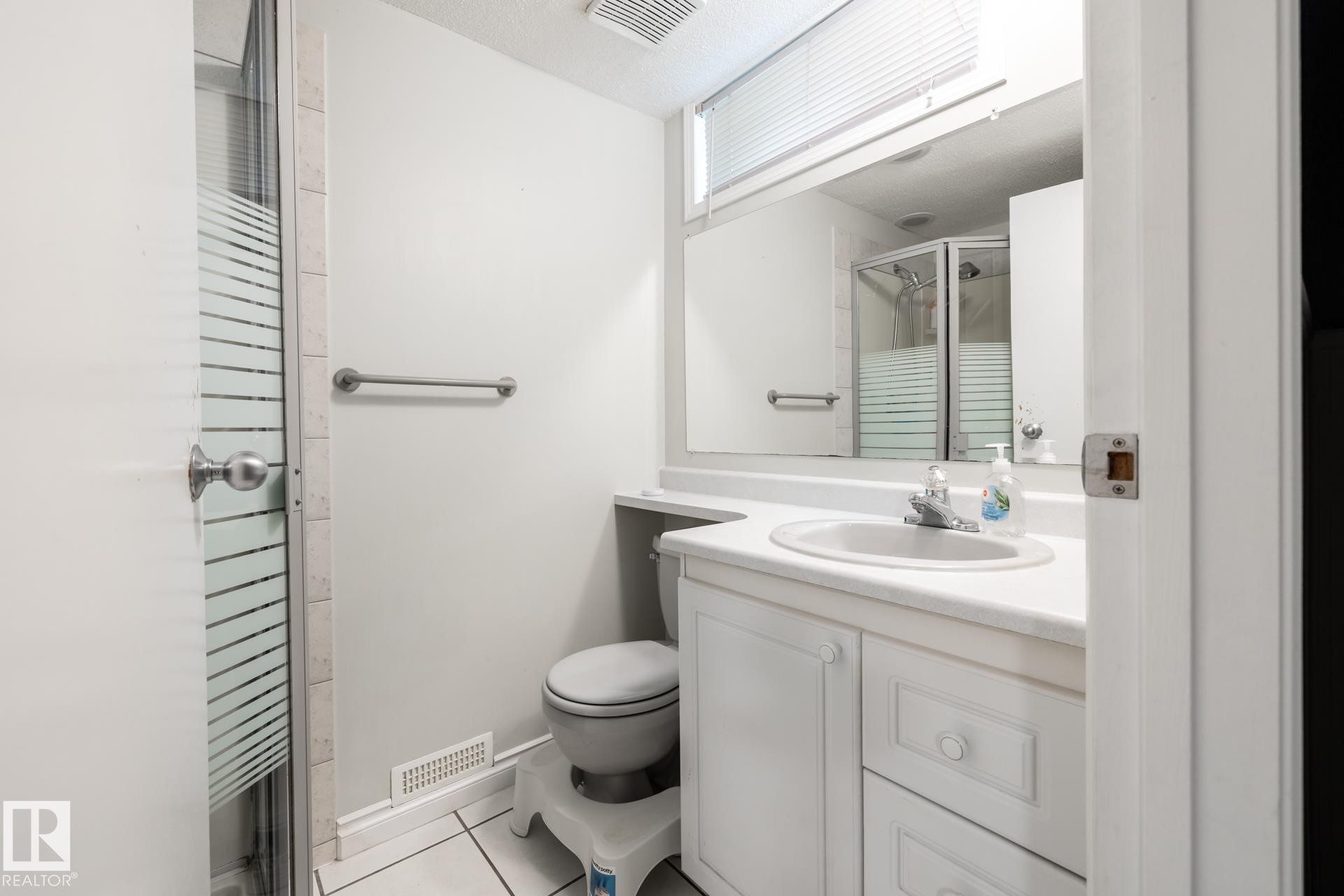 Bathroom featuring a glass-enclosed shower, white vanity with integrated sink, white tile flooring, and mirrored medicine cabinet - 27 Danforth Crescent, St. Albert, AB