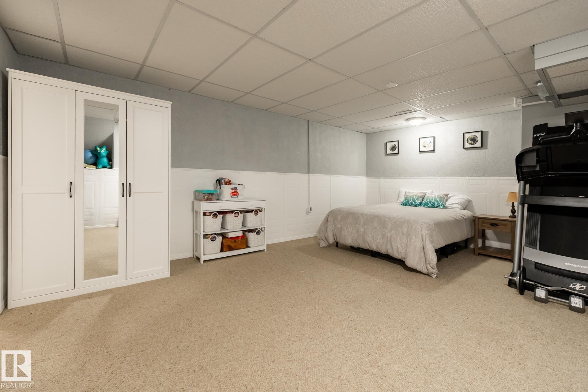 Spacious room featuring neutral carpet flooring, a white paneled wainscoting, and a drop ceiling with integrated lighting - 27 Danforth Crescent, St. Albert, AB