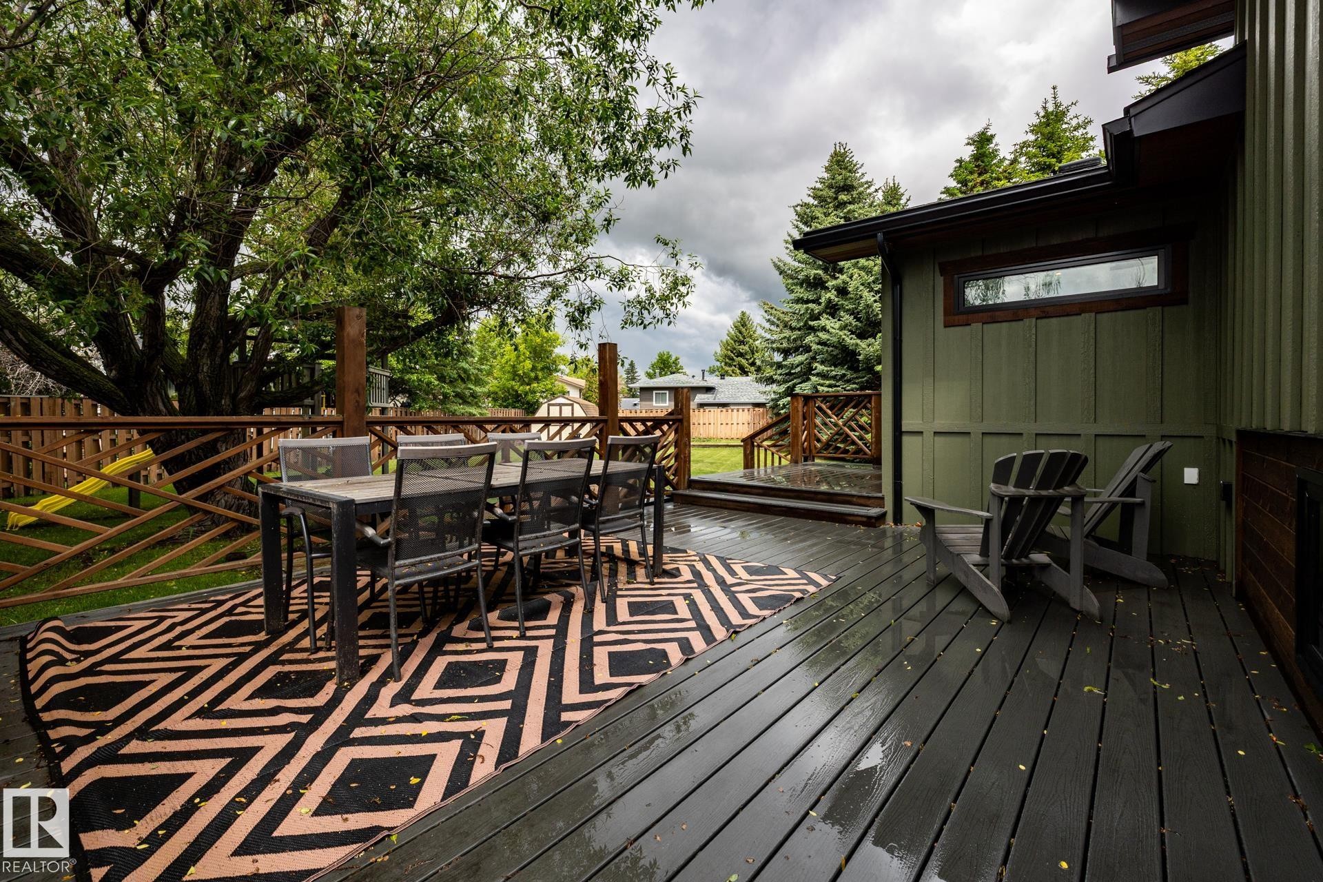 Expansive wood-finish deck with a decorative privacy fence and mature perimeter trees - 27 Danforth Crescent, St. Albert, AB