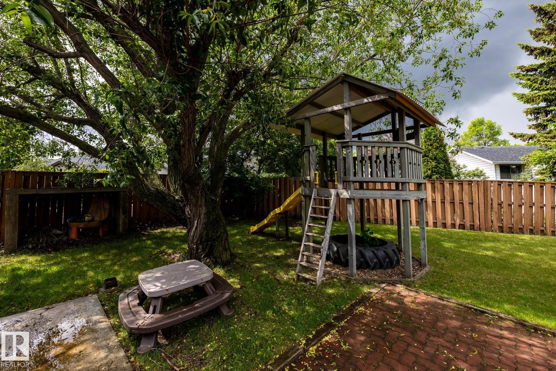 Expansive backyard featuring a lush lawn, mature shade tree, privacy fencing, and a brick paver patio area - 27 Danforth Crescent, St. Albert, AB
