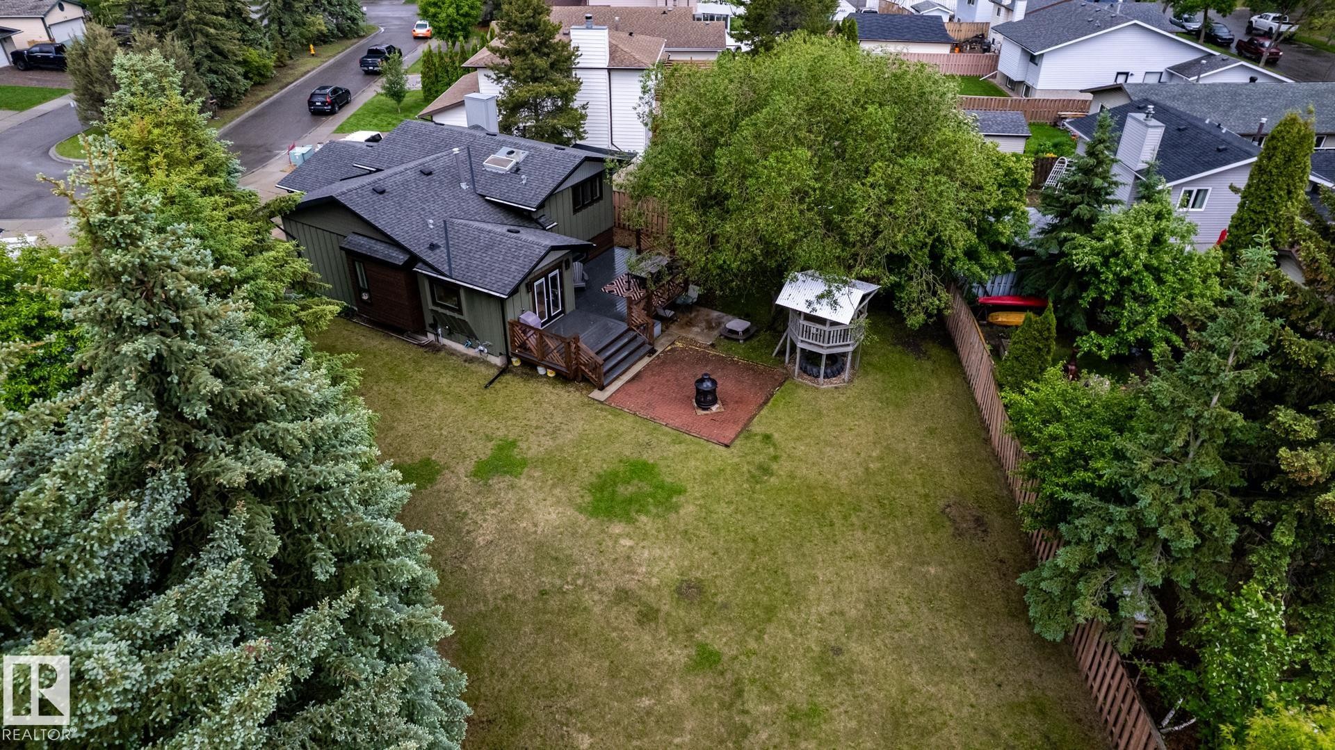 Expansive backyard featuring a large lawn area, mature trees, a multi-level deck, and a fenced perimeter - 27 Danforth Crescent, St. Albert, AB