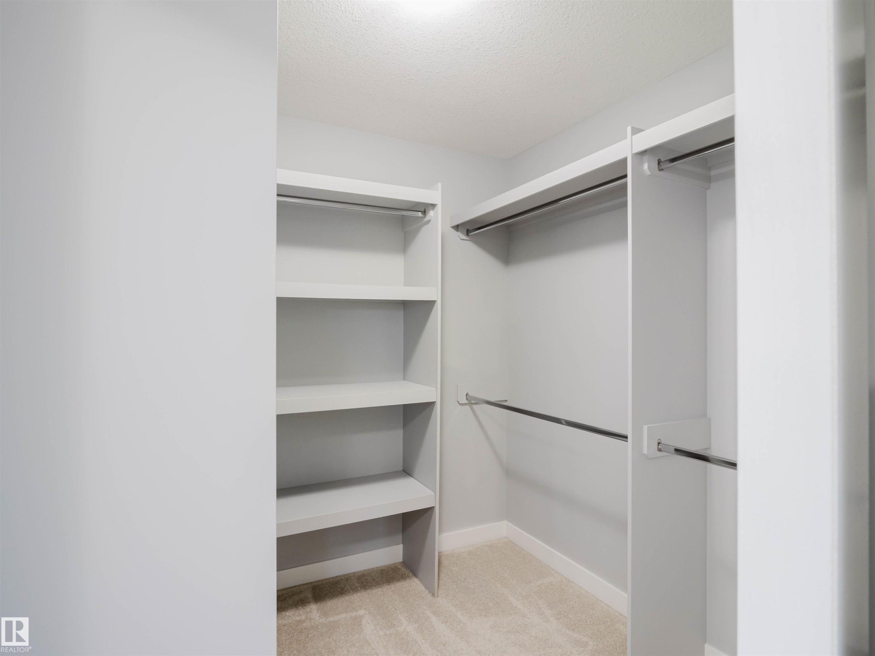 Walk-in closet featuring built-in shelving, multiple hanging rods, and neutral carpet flooring - 2526 Wonnacott Loop Sw, Edmonton, AB - Indoor With Storage