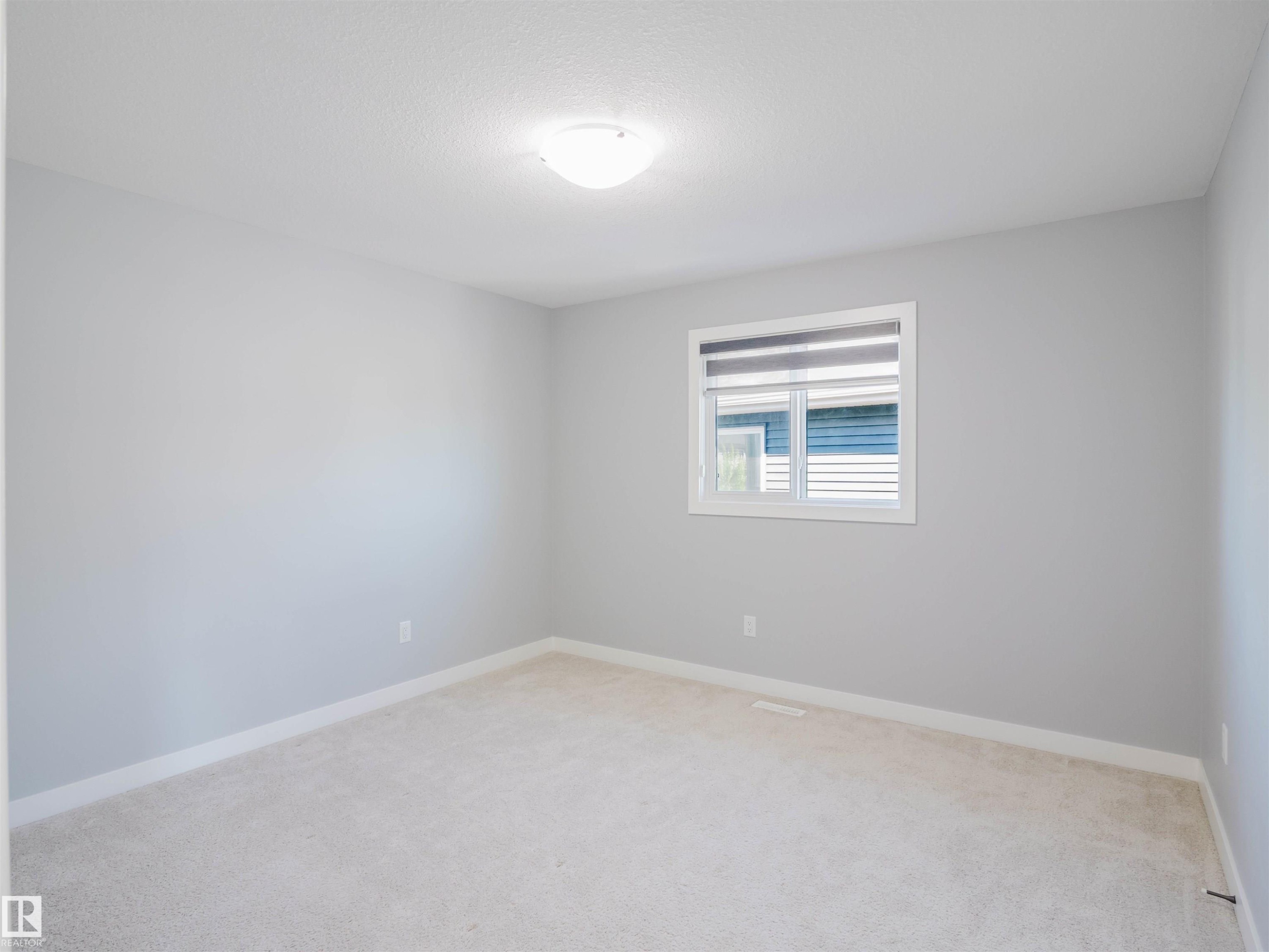 Neutral-toned room featuring a single window with blinds, light-colored carpeting, white baseboards, and a ceiling-mounted light fixture - 2526 Wonnacott Loop Sw, Edmonton, AB - Indoor Photo Showing Other Room