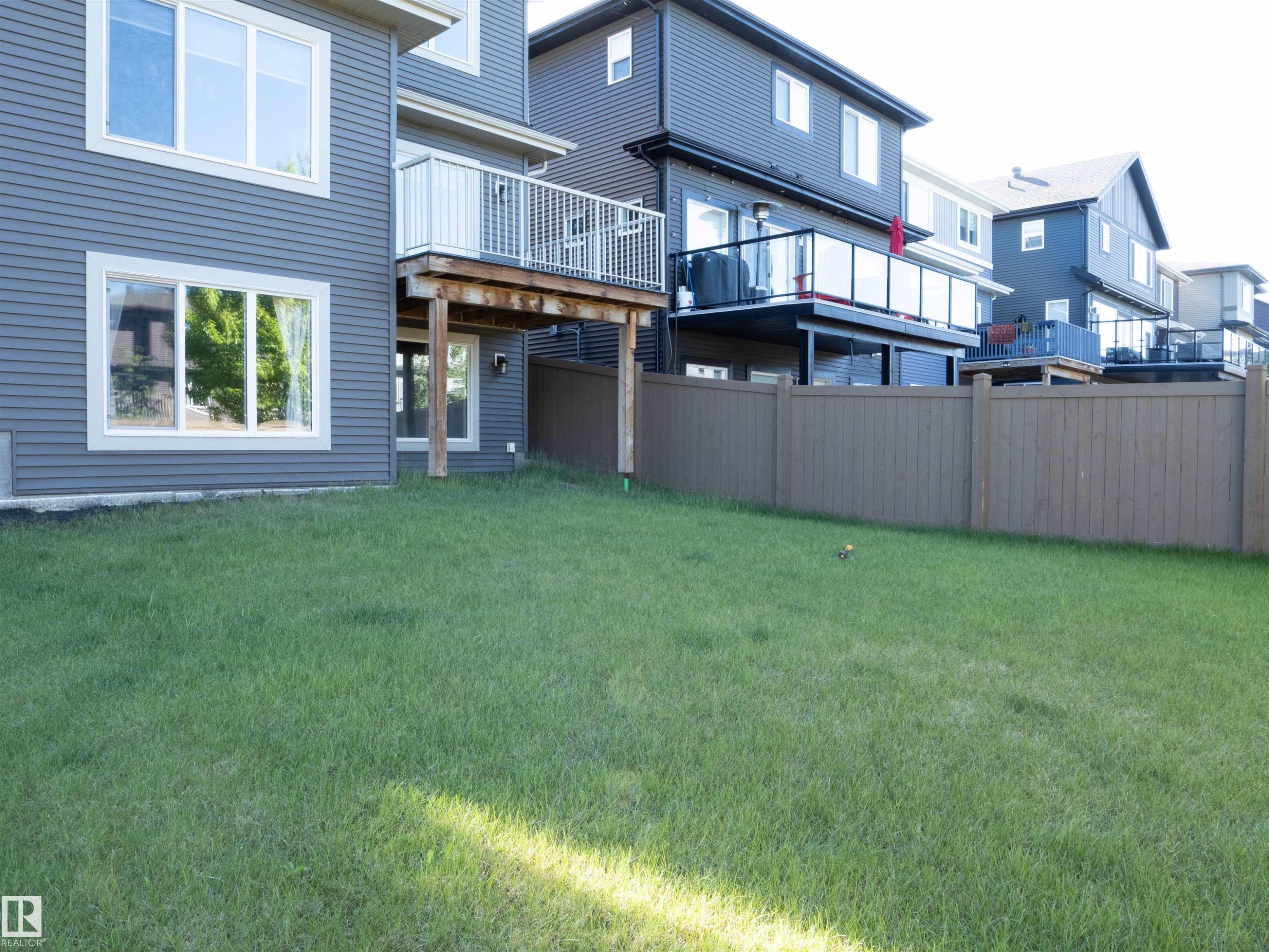 Spacious backyard featuring a grass lawn, privacy fencing, and a ground-level walkout - 2526 Wonnacott Loop Sw, Edmonton, AB - Outdoor With Deck Patio Veranda
