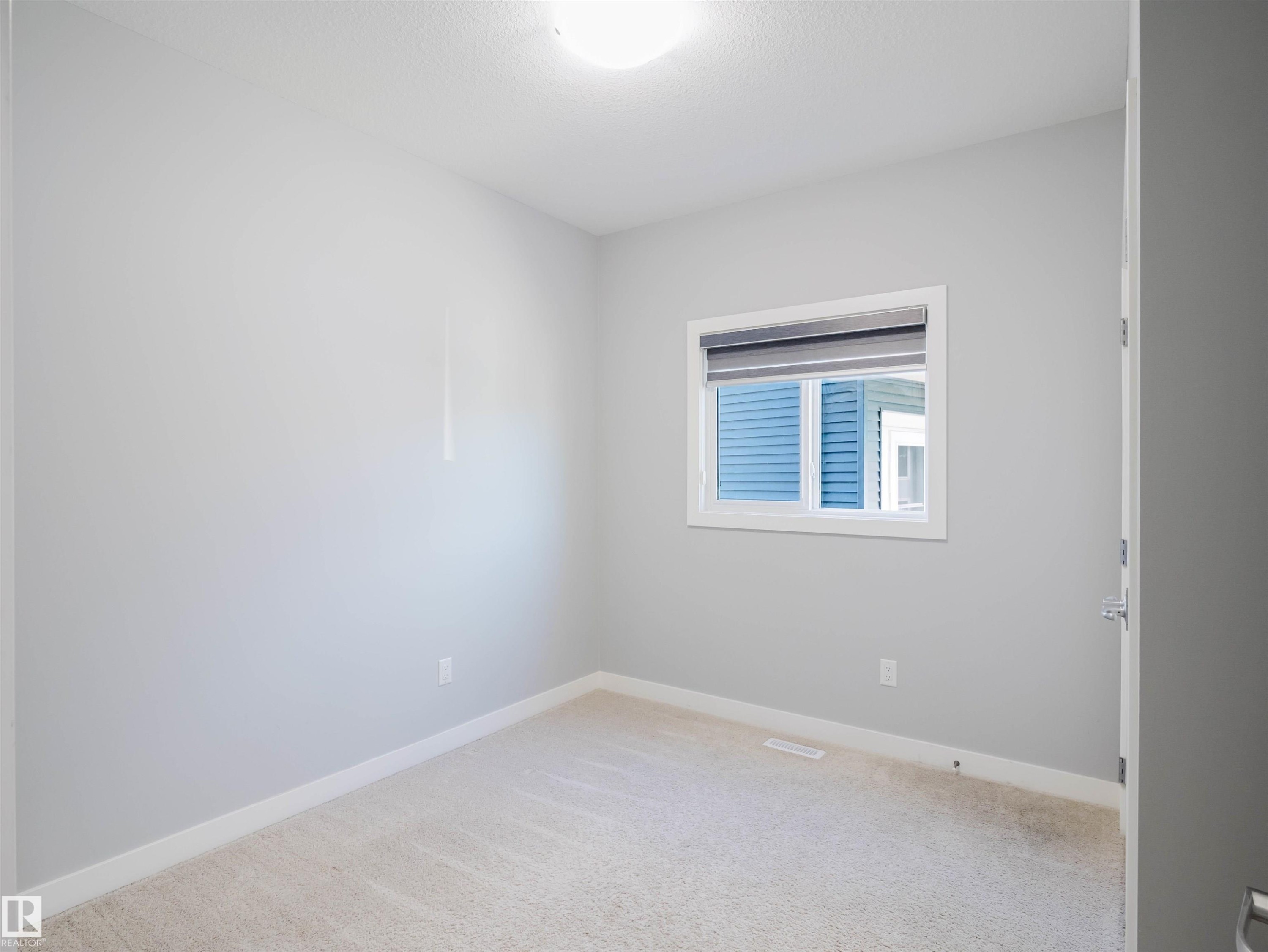 Neutral-toned room featuring a single window with a privacy blind, light-colored carpeting, white baseboards, and a flush-mount ceiling light - 2526 Wonnacott Loop Sw, Edmonton, AB - Indoor Photo Showing Other Room