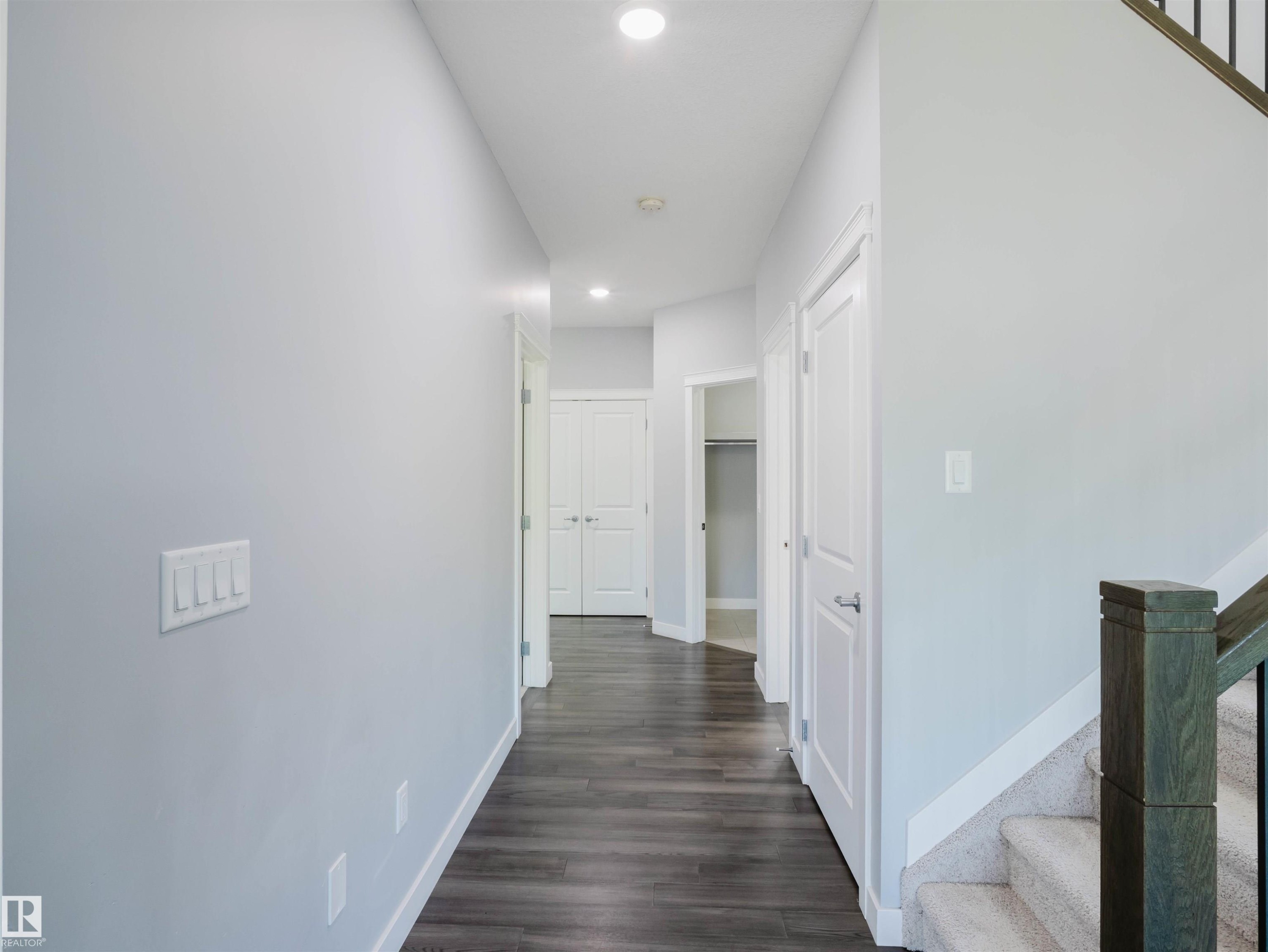 Hallway featuring wood-finish flooring, recessed lighting, neutral wall paint, white trim, and doors with brushed nickel hardware - 2526 Wonnacott Loop Sw, Edmonton, AB - Indoor Photo Showing Other Room