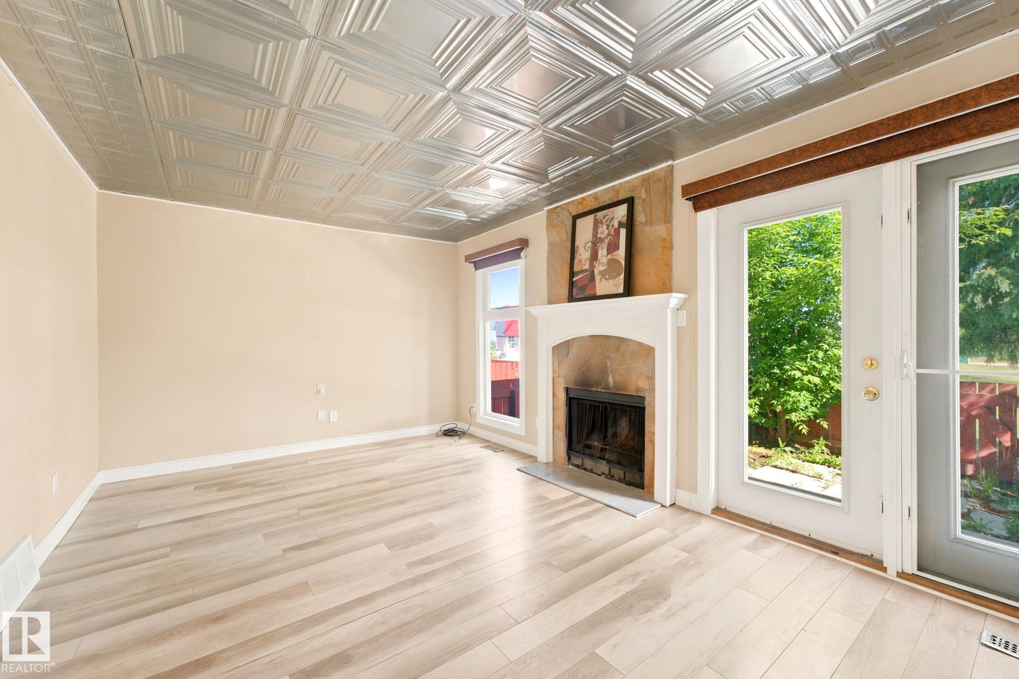Living area featuring a pressed metal ceiling, a fireplace with a stone surround and white mantel, and wood-finish flooring - #41 4707 126 Av Nw, Edmonton, AB